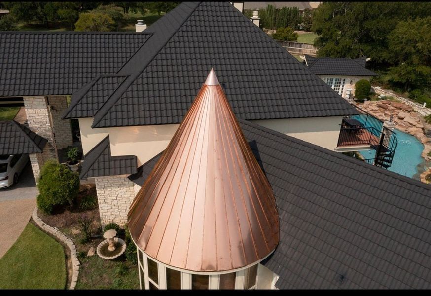 An aerial view of a home with a large, polished copper cone-shaped roof turret and dark grey textured shingle roofing.