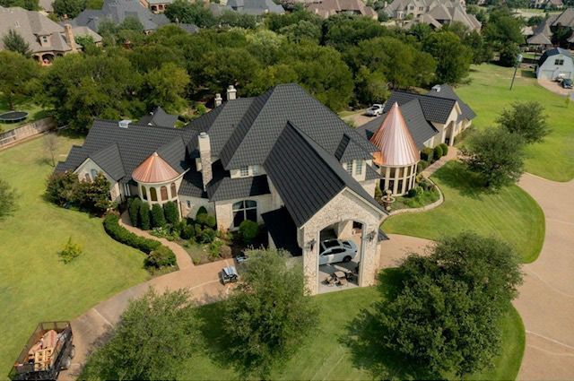 Aerial view of a large stone mansion with a dark metal roof, copper turrets, and a spacious landscaped lawn.