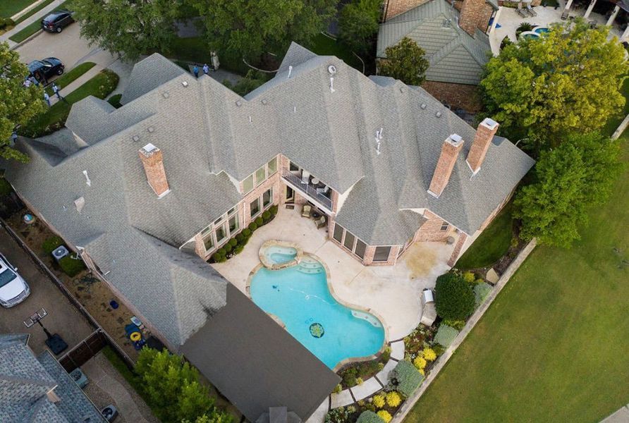 Aerial view of a large residential home with a grey roof, surrounding pool deck, and kidney-shaped swimming pool.