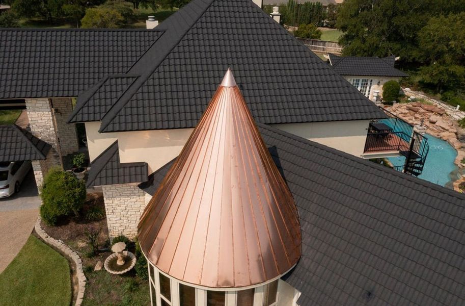Aerial view of a house with a dark metal shingle roof and a prominent, conical copper turret.