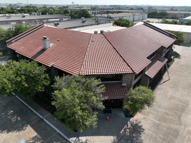 Aerial view of a commercial building with a terracotta-colored tiled roof and adjacent paved parking lots.