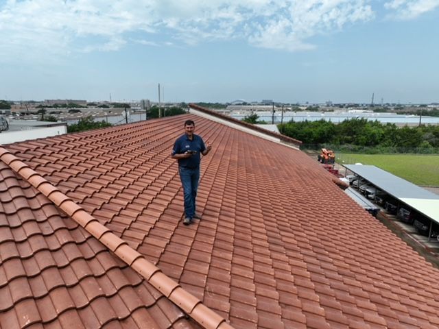 A person stands on a large, red-tiled roof during an inspection, overlooking an industrial outdoor area.