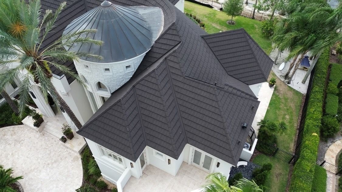 High-angle view of a white, multi-story house with a dark, textured tile roof and a circular turret.