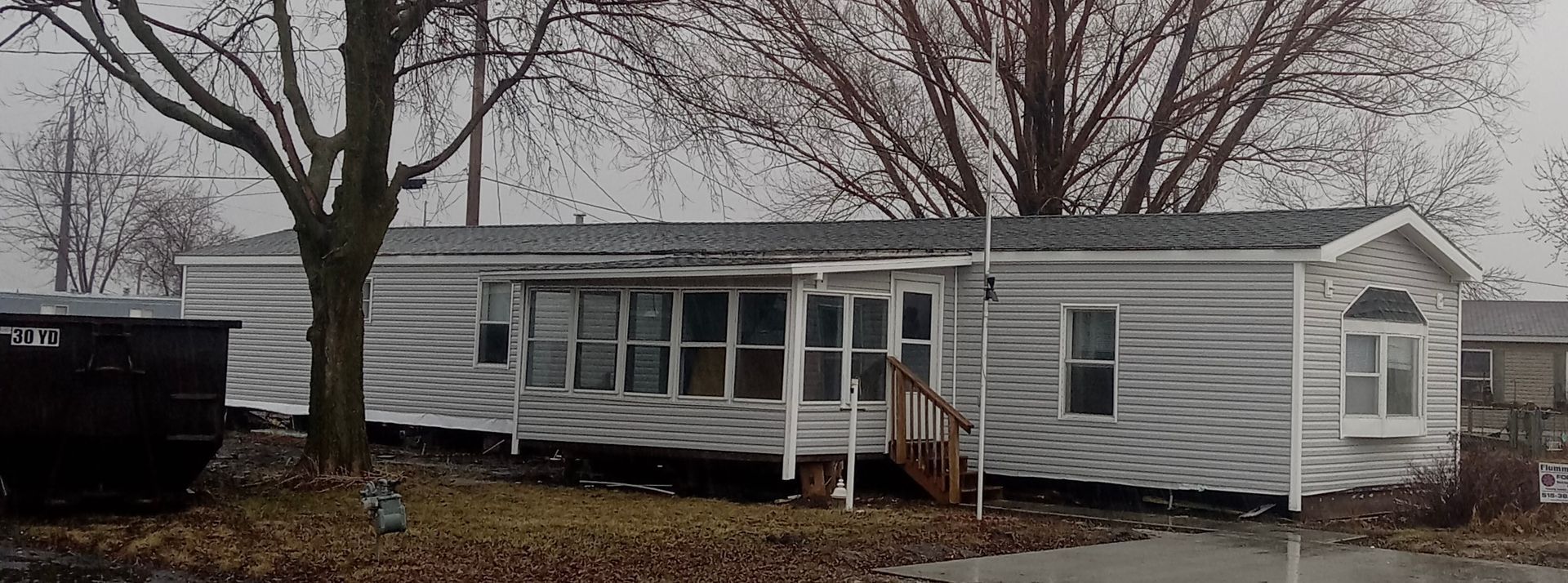 A small, light-blue house with white trim and a small porch on a grassy lot under a partly cloudy sky.