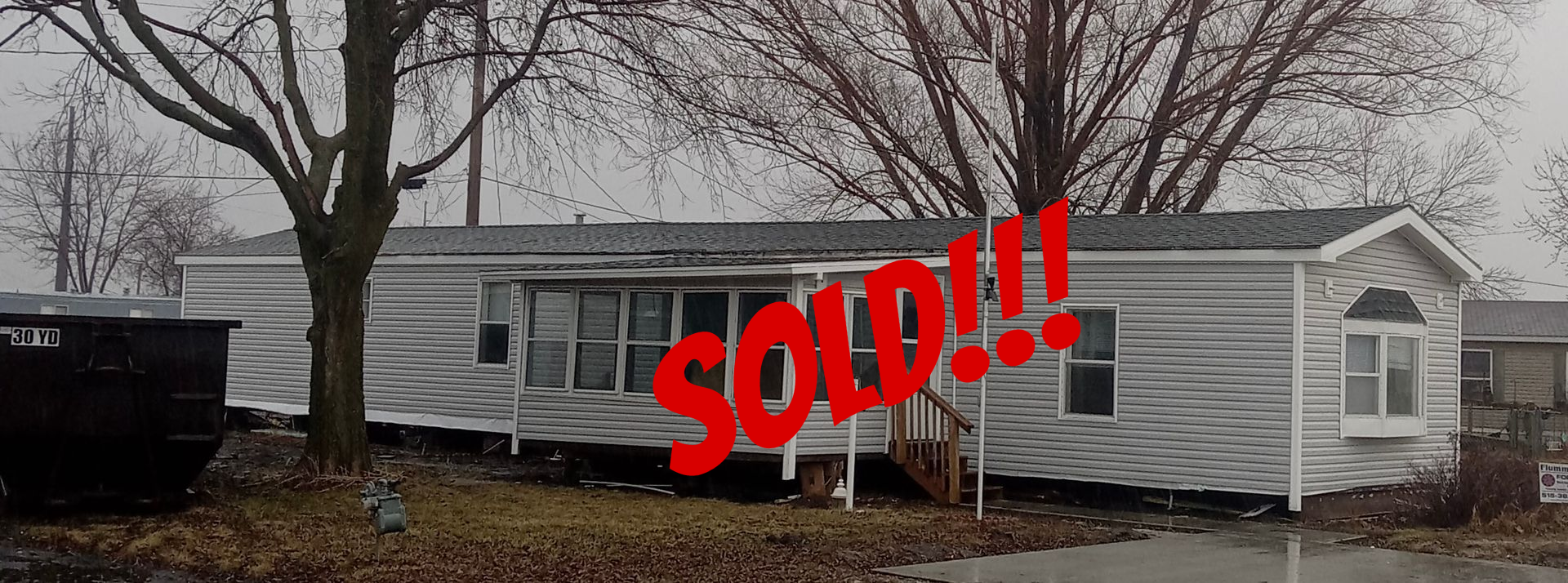 A small, light-blue house with white trim and a small porch on a grassy lot under a partly cloudy sky.