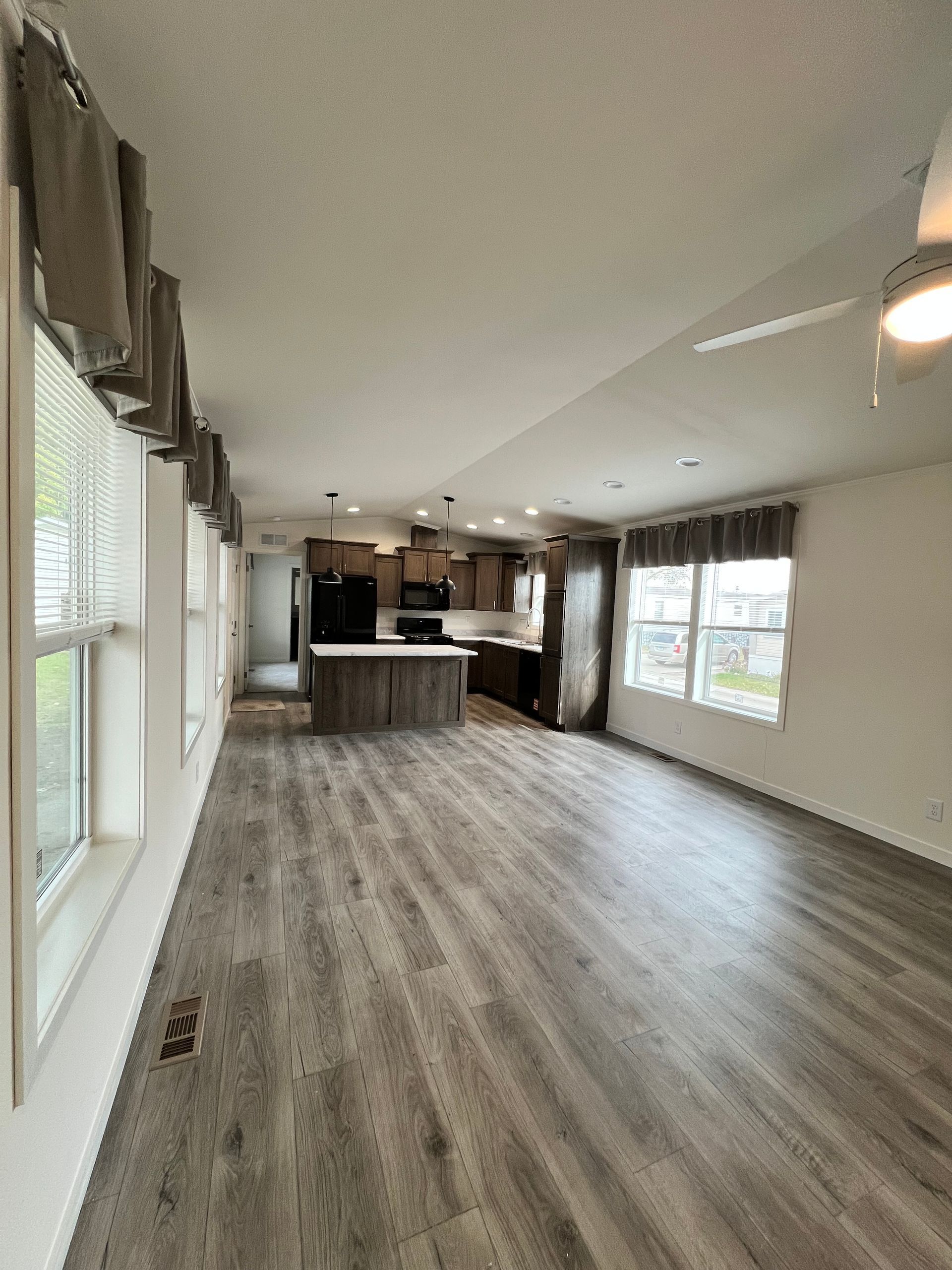 Interior of a modern kitchen and living room. Features include wood floors, windows, and an island.