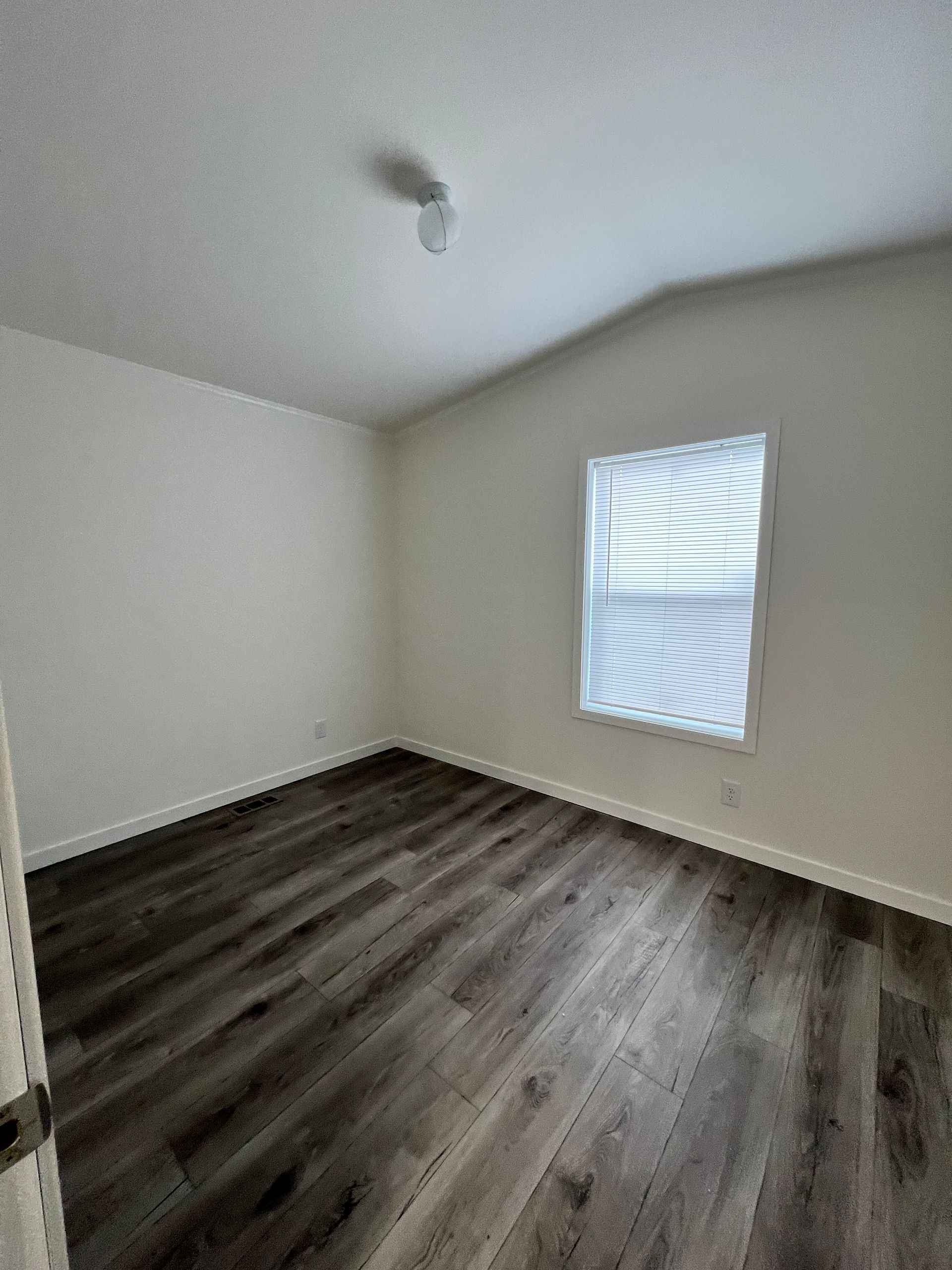 Empty room with gray wood-look flooring, white walls, small window, and ceiling light fixture.