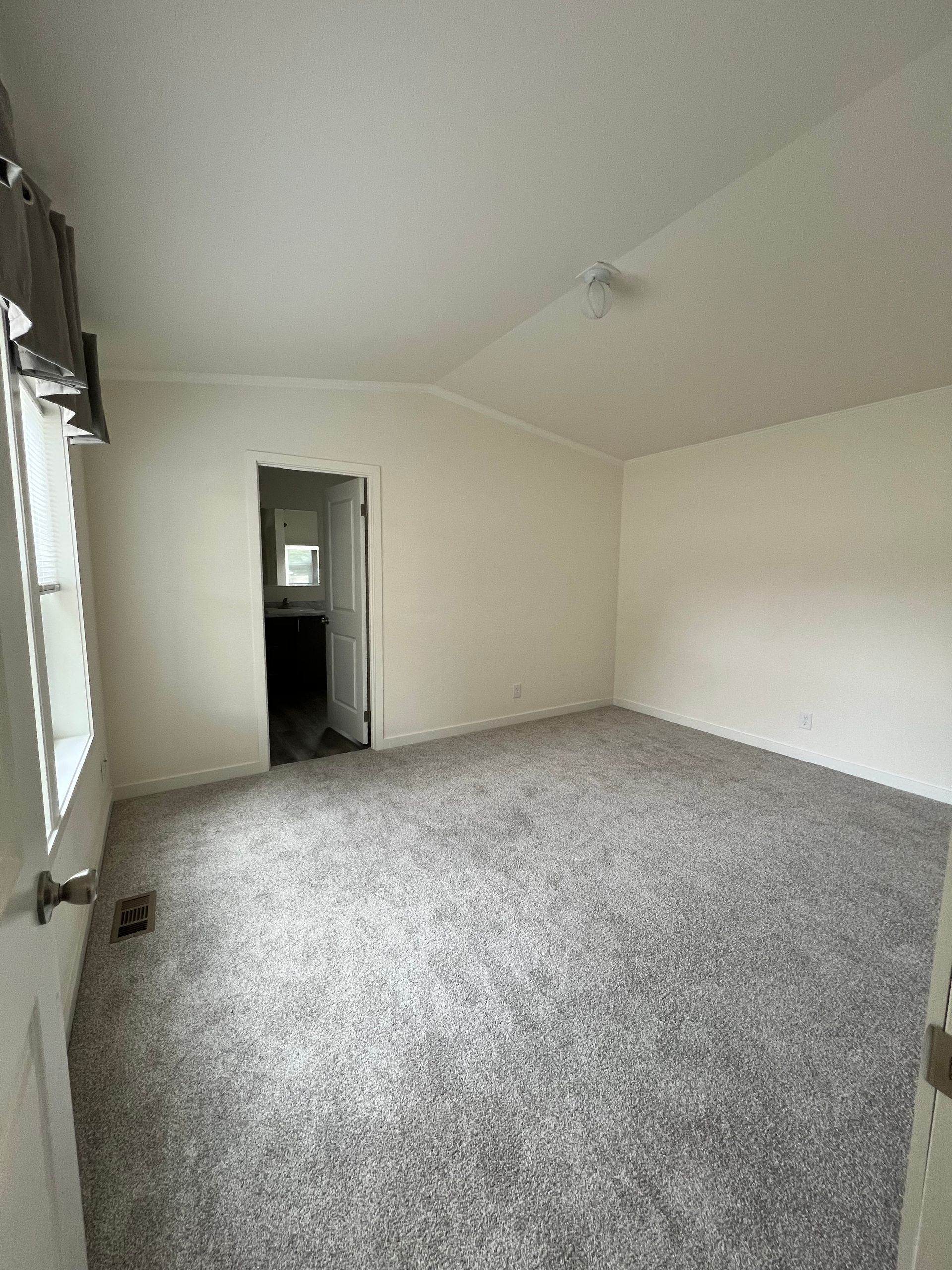Empty room with gray carpet, off-white walls, and a doorway leading to a dark area.