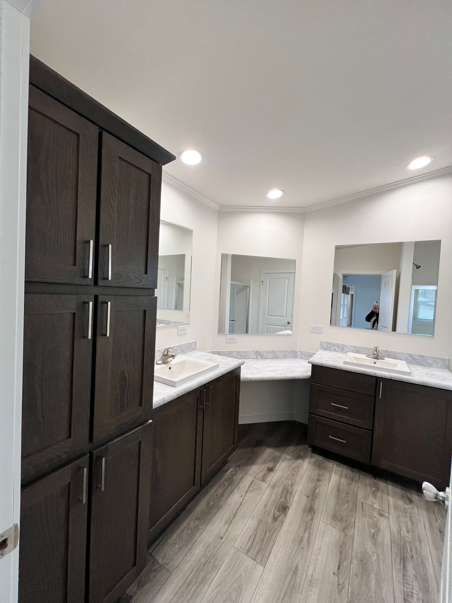 Bathroom with dark brown cabinets, two vanities, and a built-in makeup area. Light wood-look flooring.
