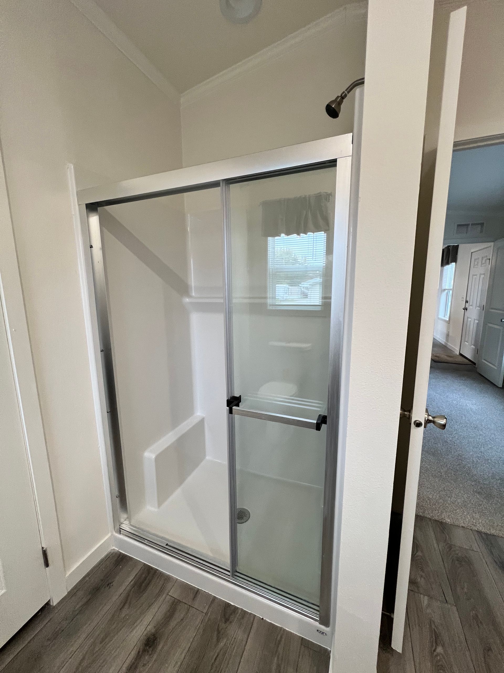 Shower stall with sliding glass doors, in a bathroom. White walls, grey floor.