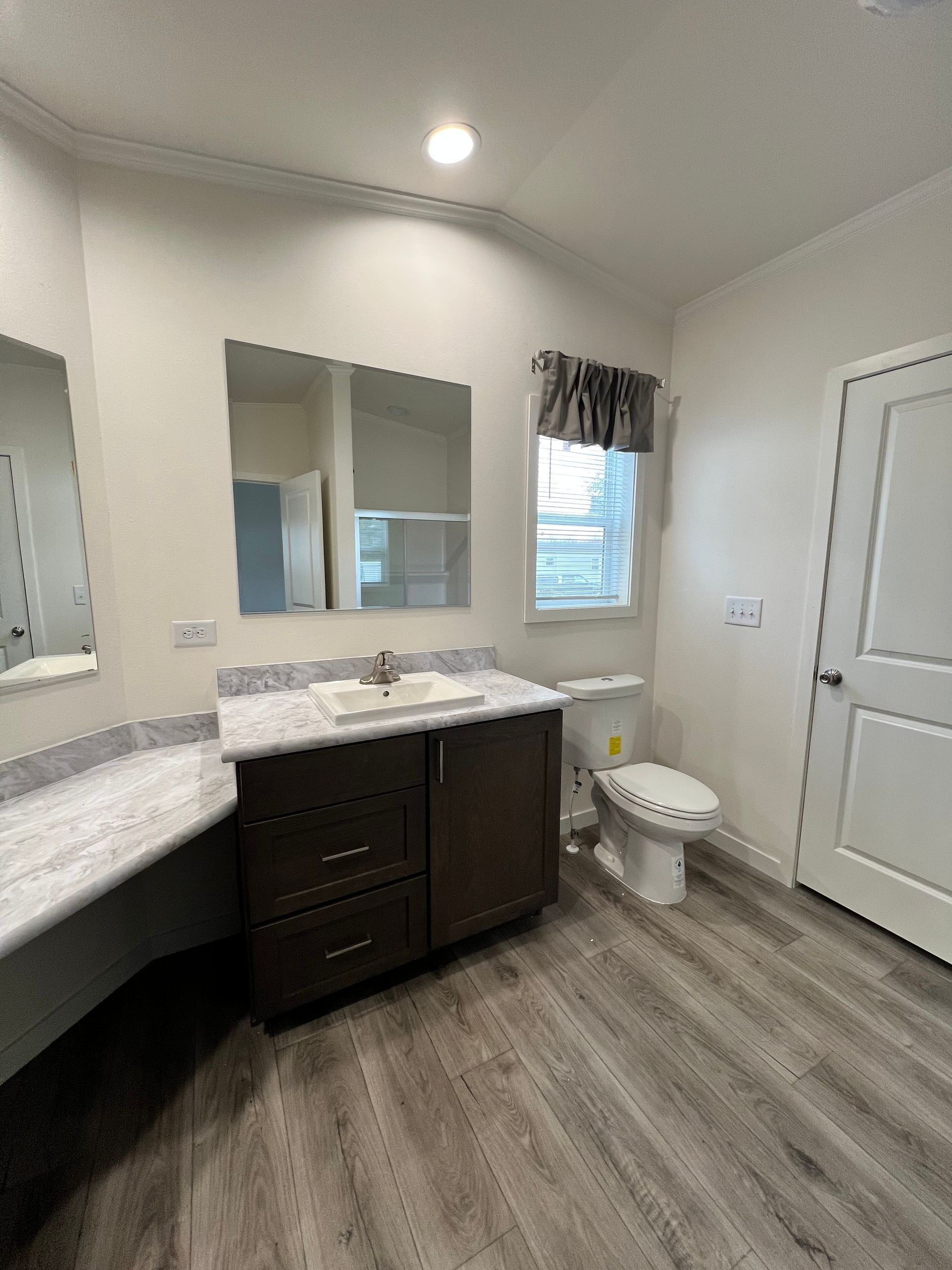 Bathroom with a vanity, toilet, and window with a curtain. Wood-look flooring.