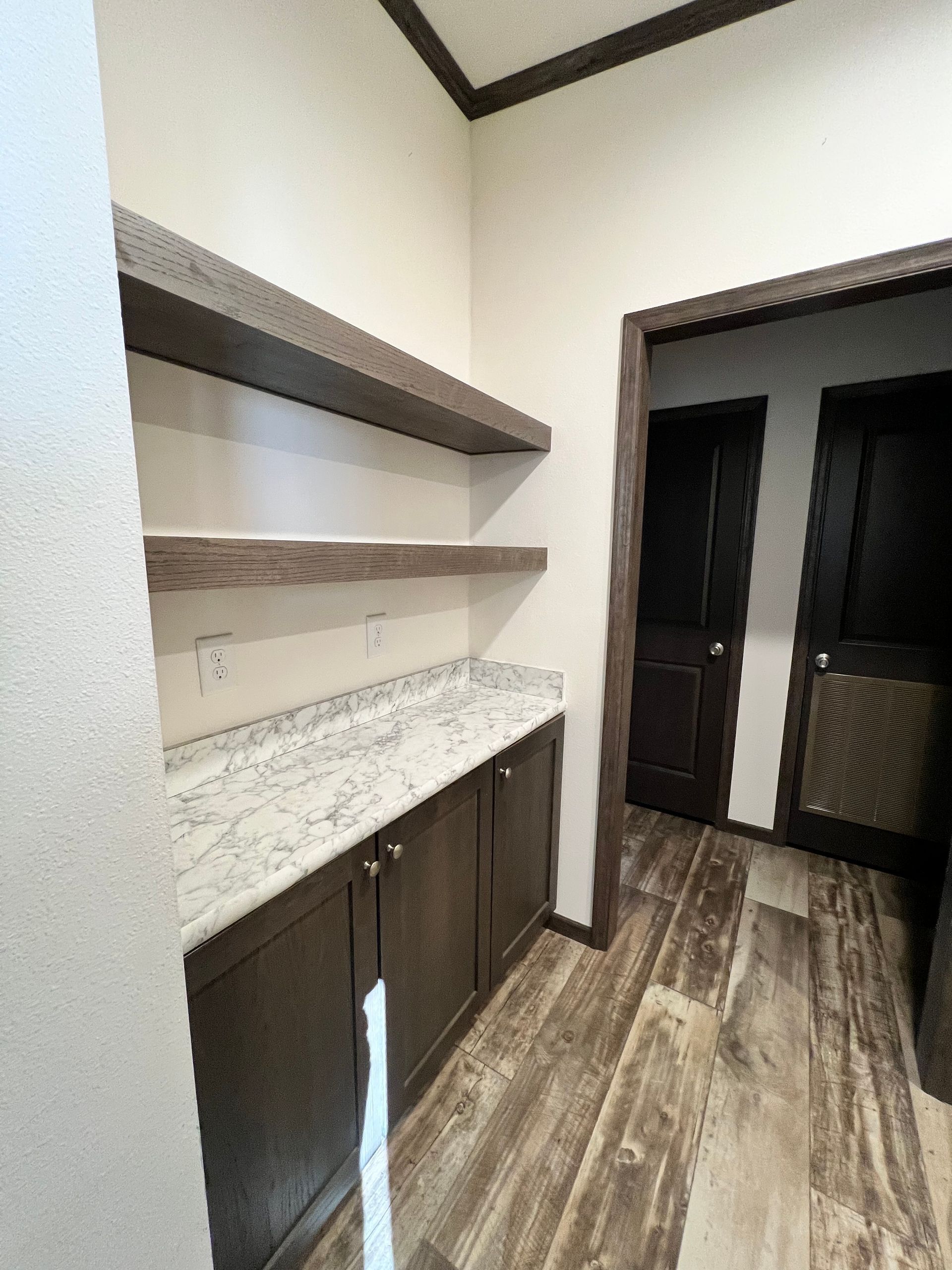 Pantry with wood shelves, granite countertop, and dark cabinets. Doorway and wood flooring visible.