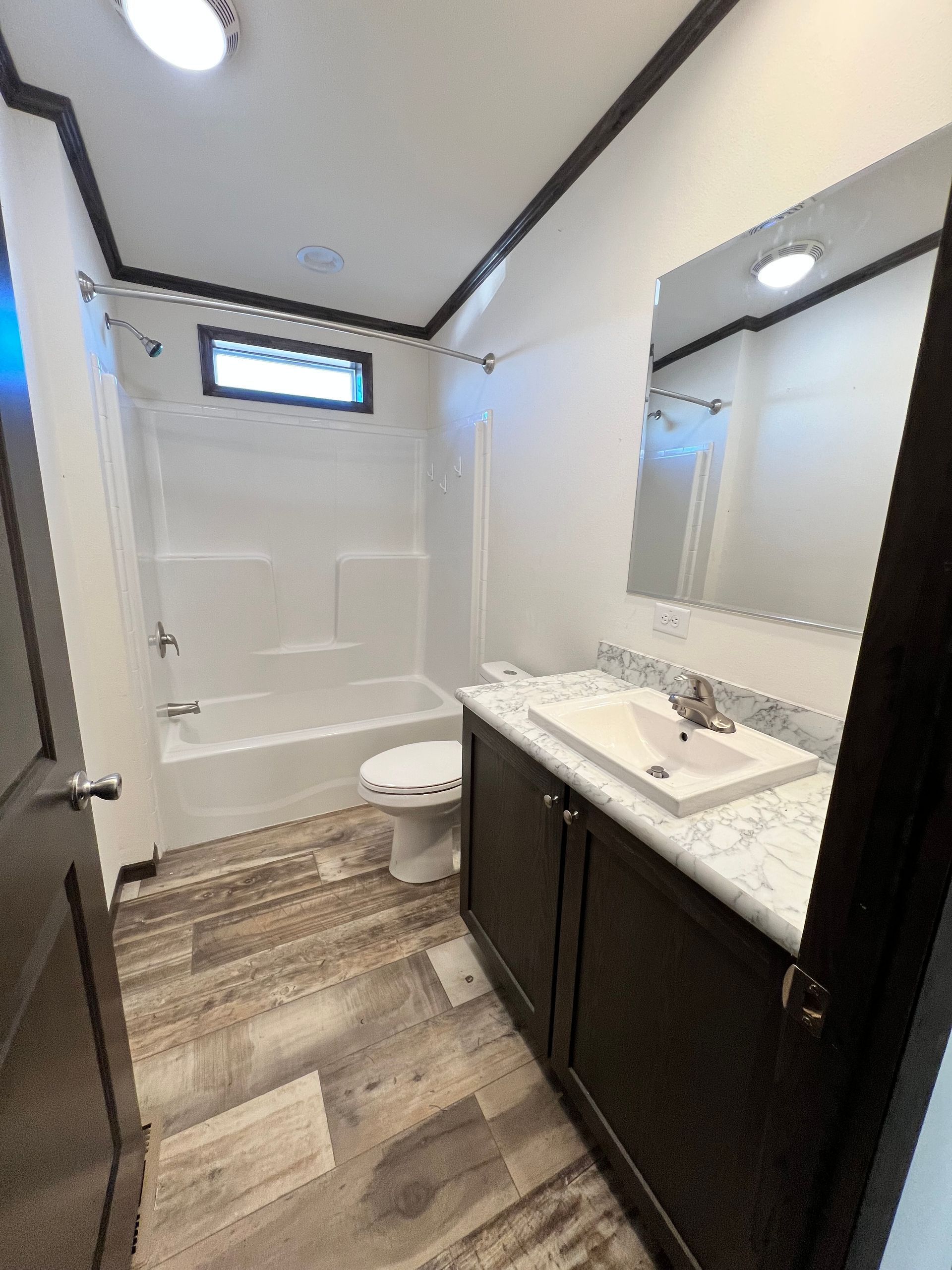 Bathroom with white tub/shower, dark vanity, light countertops, and wood-look flooring.