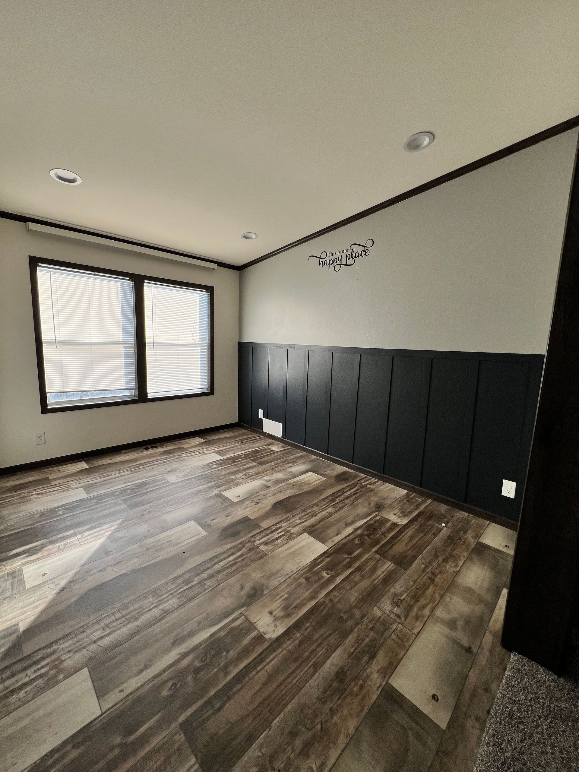 Empty room with wood-look floor, black wall paneling, white walls, and a window with blinds.
