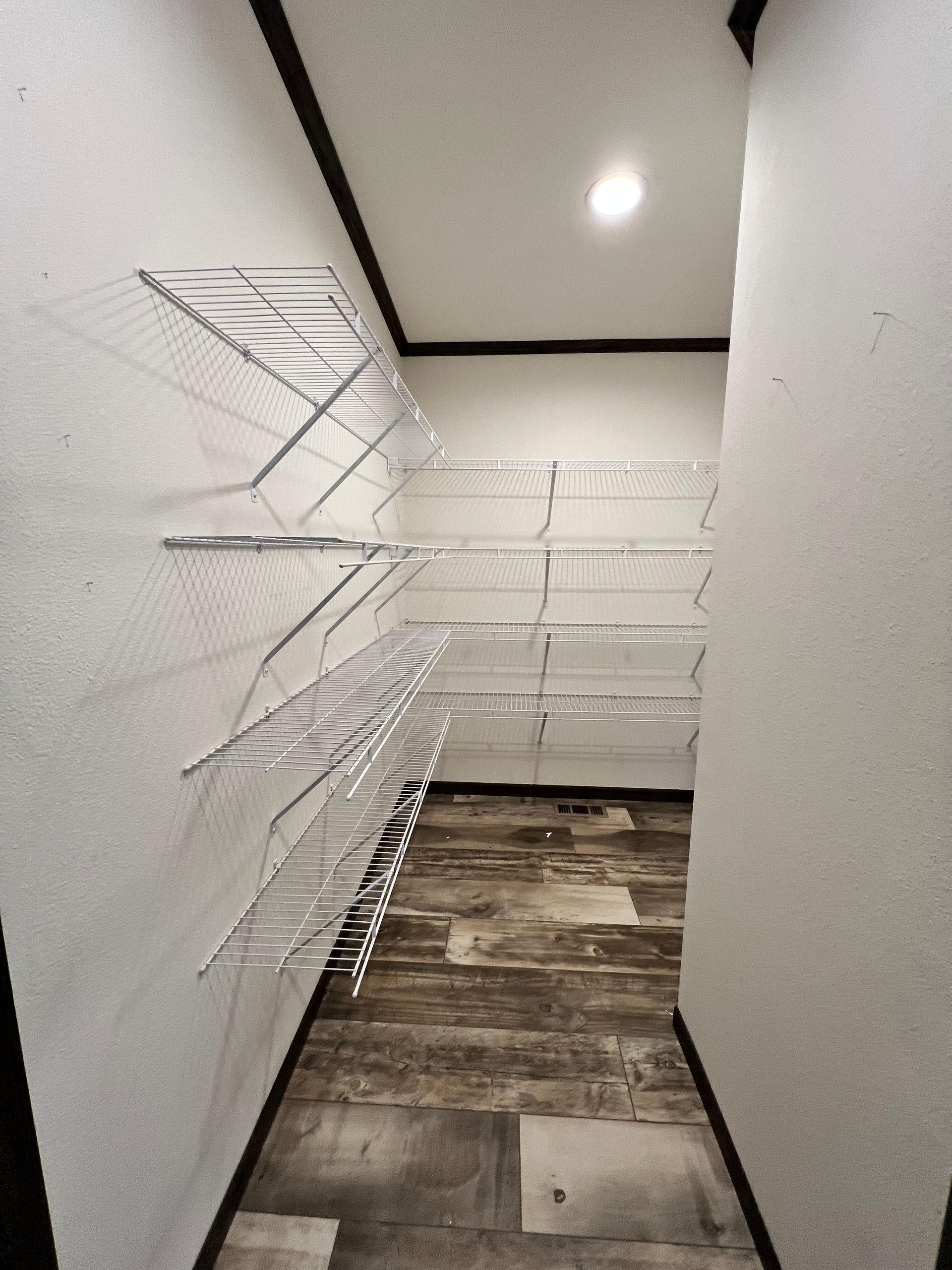 Empty walk-in closet with wire shelving on white walls and wood-look flooring.