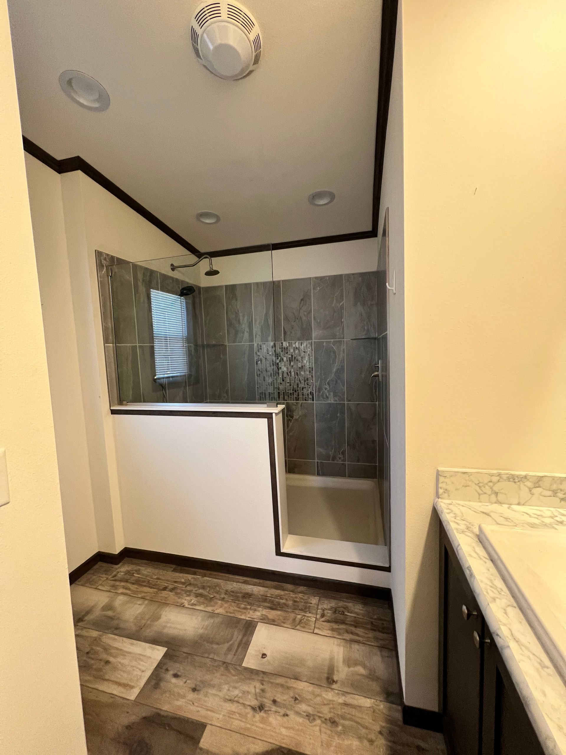Bathroom with gray tiled shower, white half-wall, wood-look floor, and beige walls.