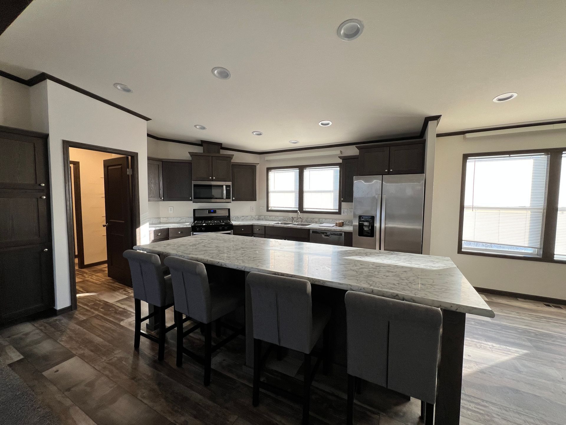Spacious kitchen with island seating, dark cabinets, stainless steel appliances, and large windows.