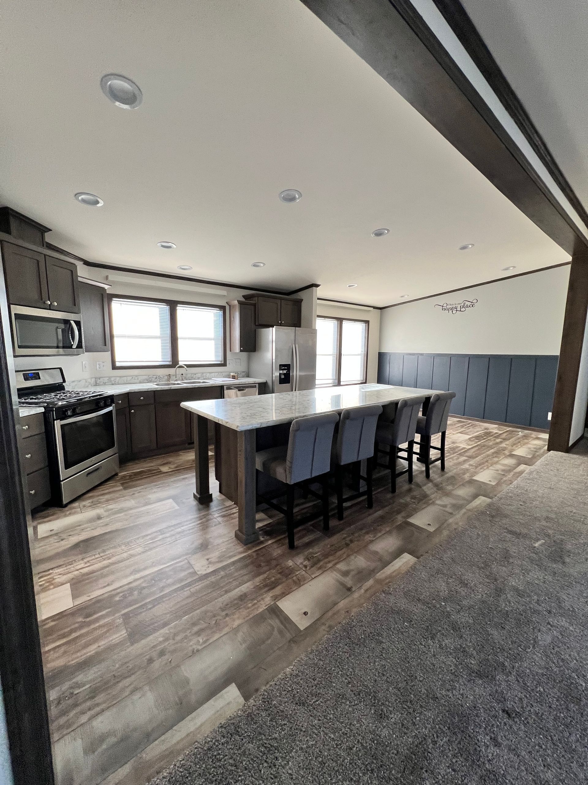 Kitchen with dark gray cabinets, a large island with seating, stainless steel appliances, and wood-look flooring.