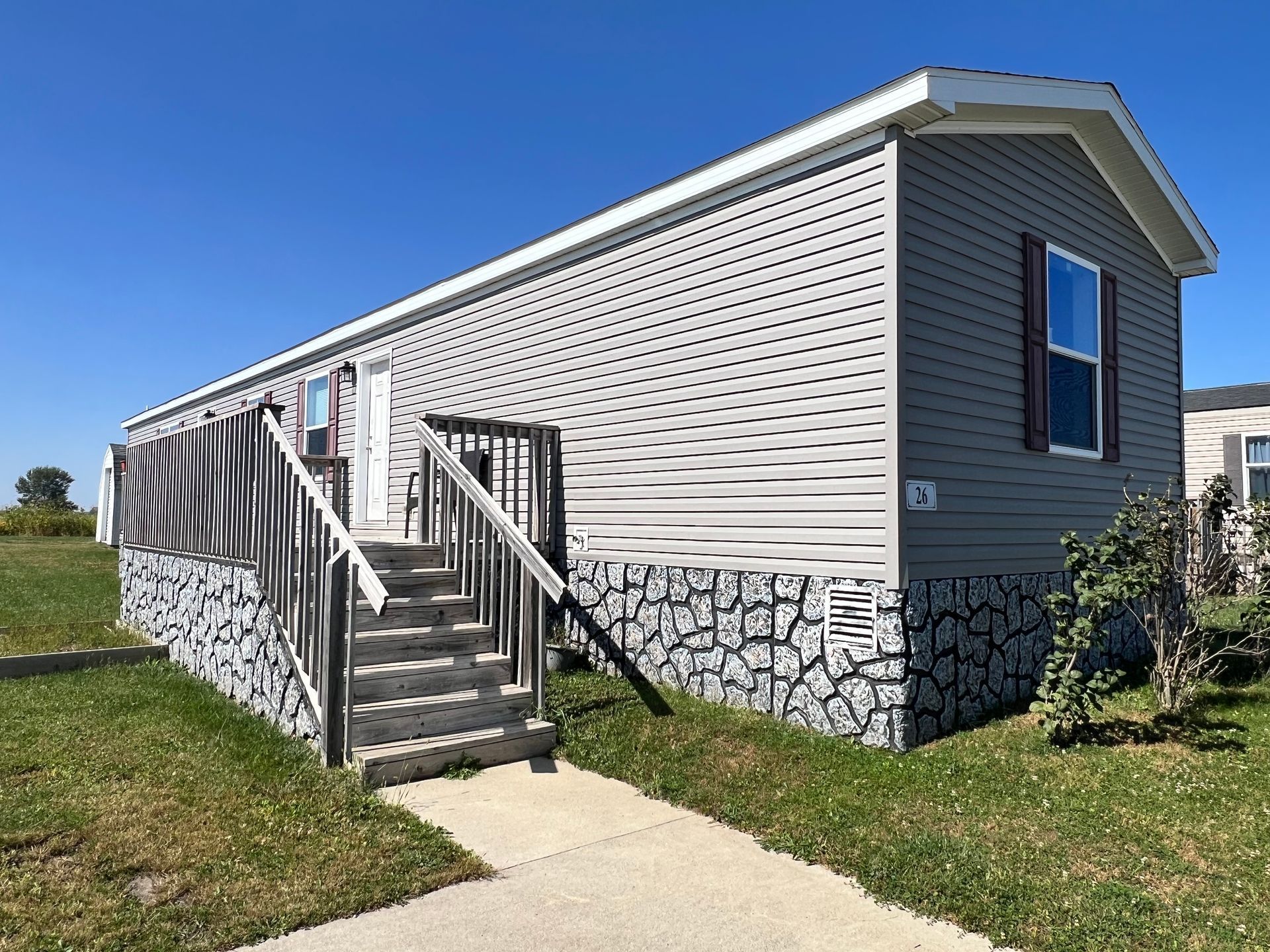 Mobile home with stone facade and steps leading to the entrance, under a blue sky.