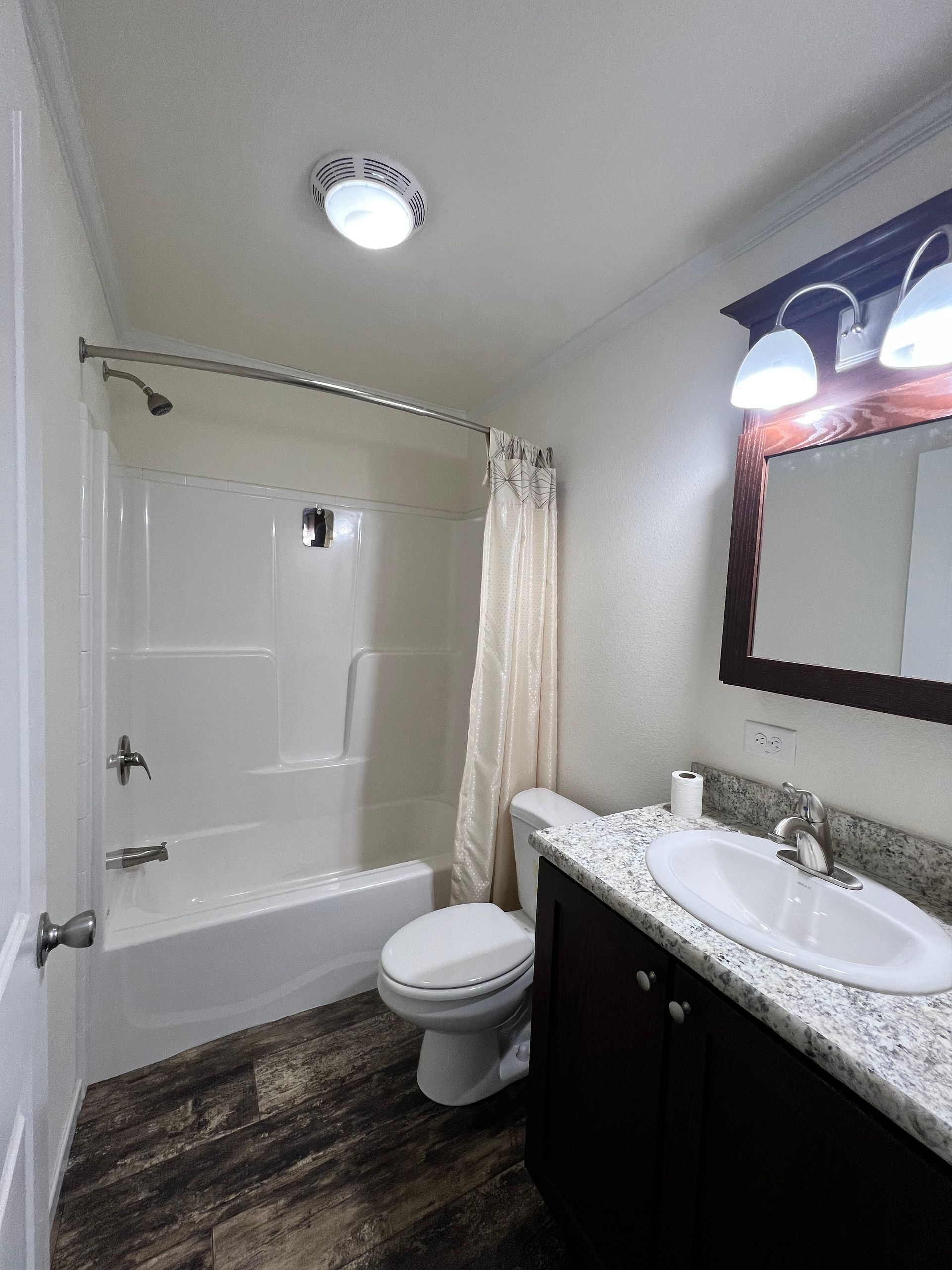 Bathroom with shower/tub, toilet, sink, and dark wood-look flooring. White and brown color scheme.
