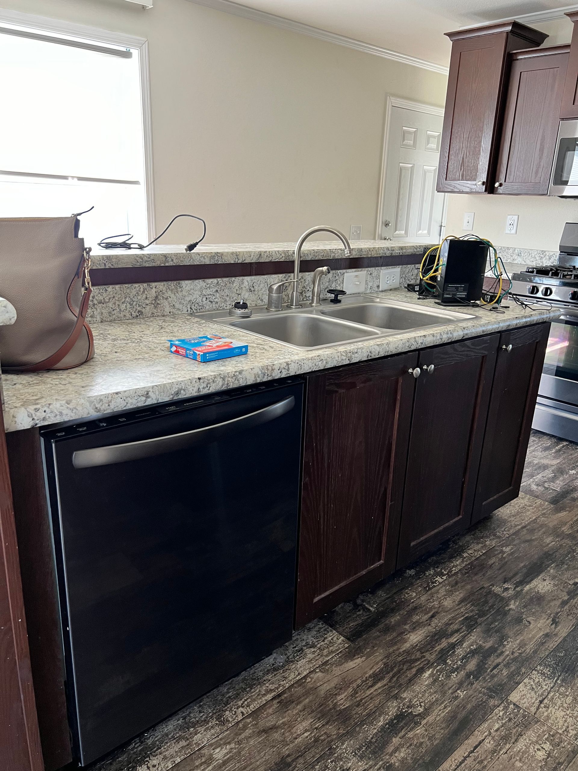 Kitchen with a black dishwasher, brown cabinets, granite countertops, and a double sink.