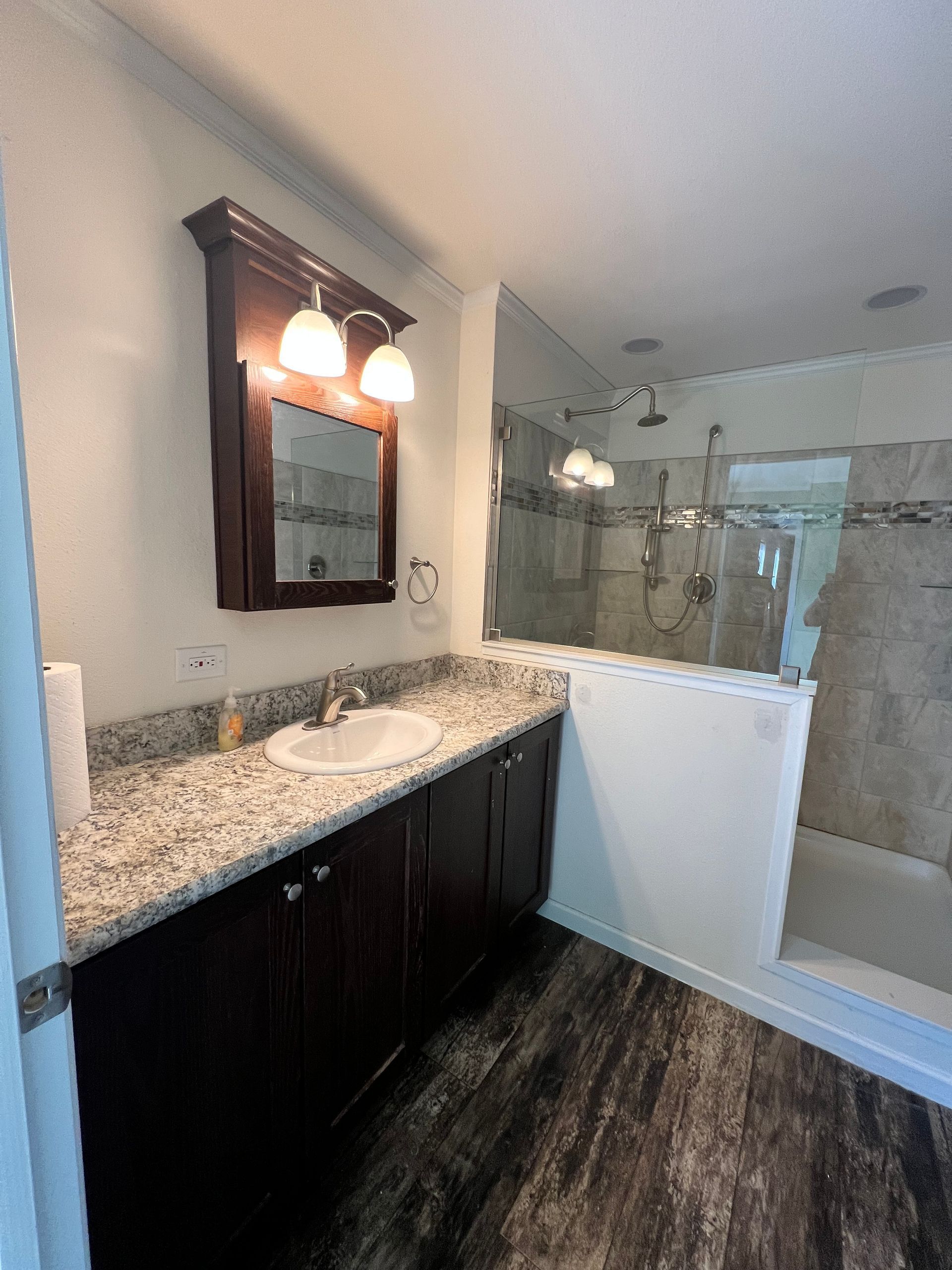 Bathroom with dark wood cabinets, granite countertop, mirror, and shower.