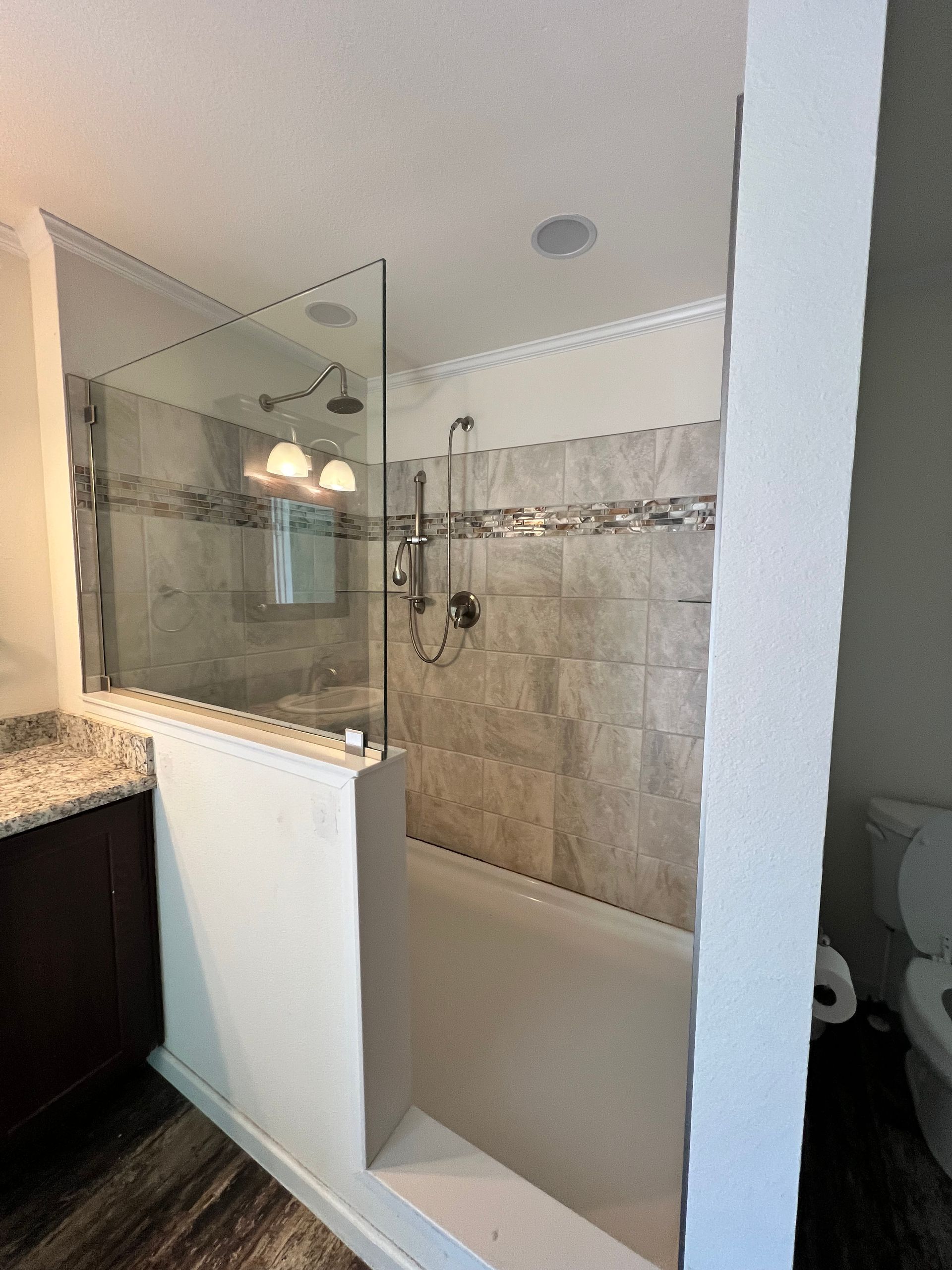 Bathroom with glass shower, tiled walls, and a built-in bench. Dark wood vanity and a toilet are visible.