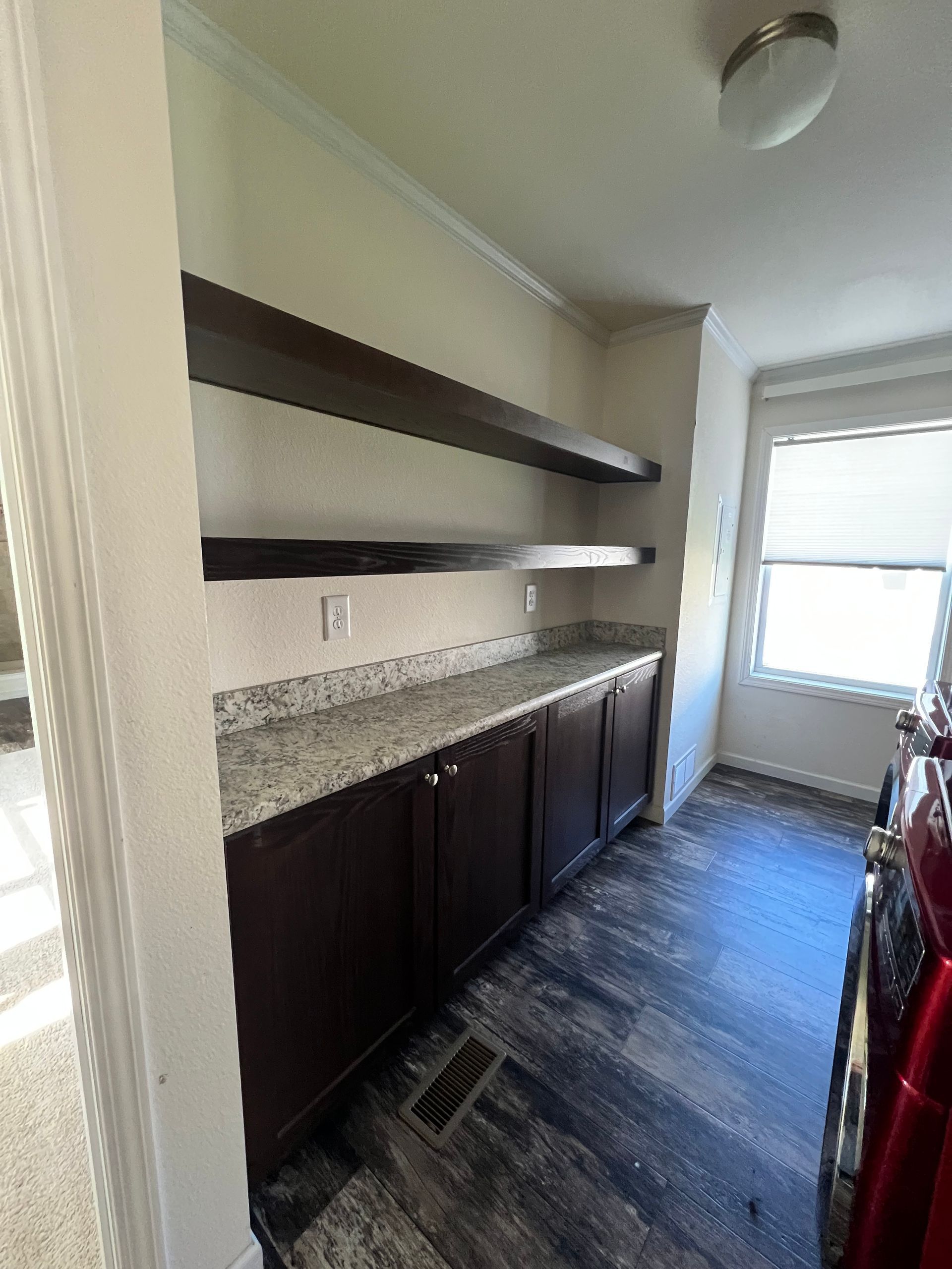 Interior pantry with dark brown cabinets, shelves, and granite countertop; window on the right.
