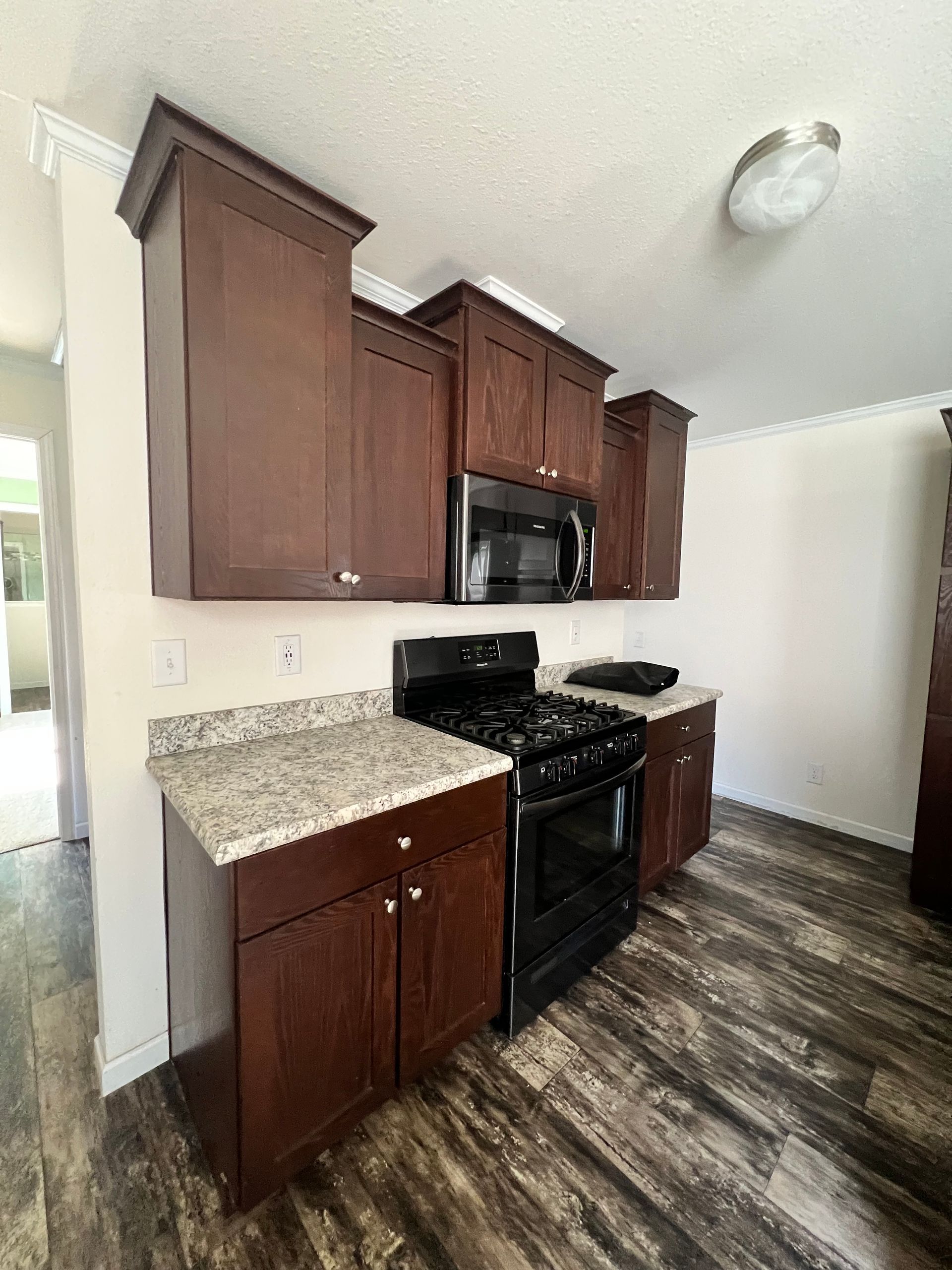 Kitchen with dark brown cabinets, black stove, granite countertops, and wood-look flooring.