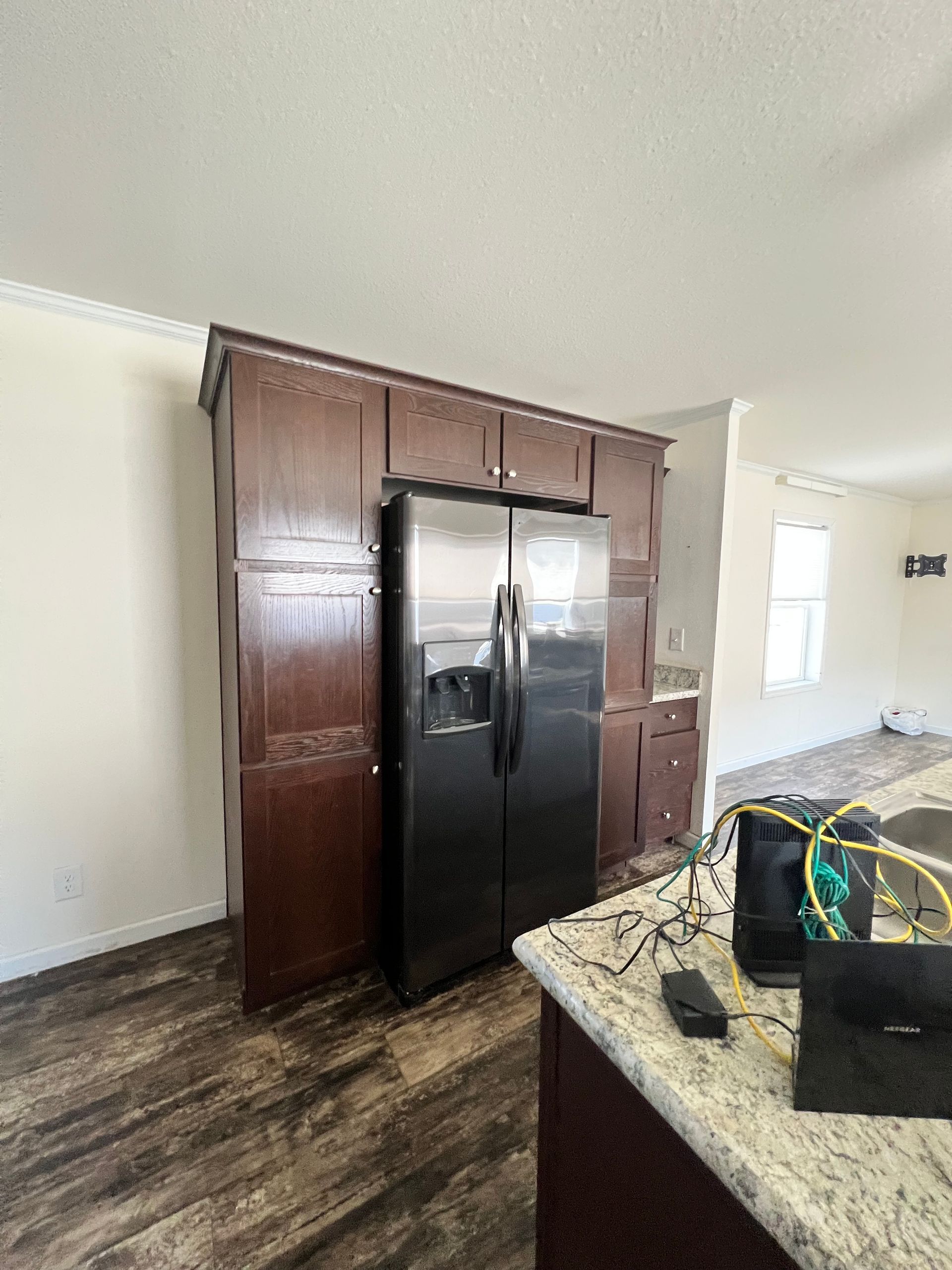 Dark cabinets surround a stainless steel refrigerator in a kitchen with wood-look flooring and a light countertop.