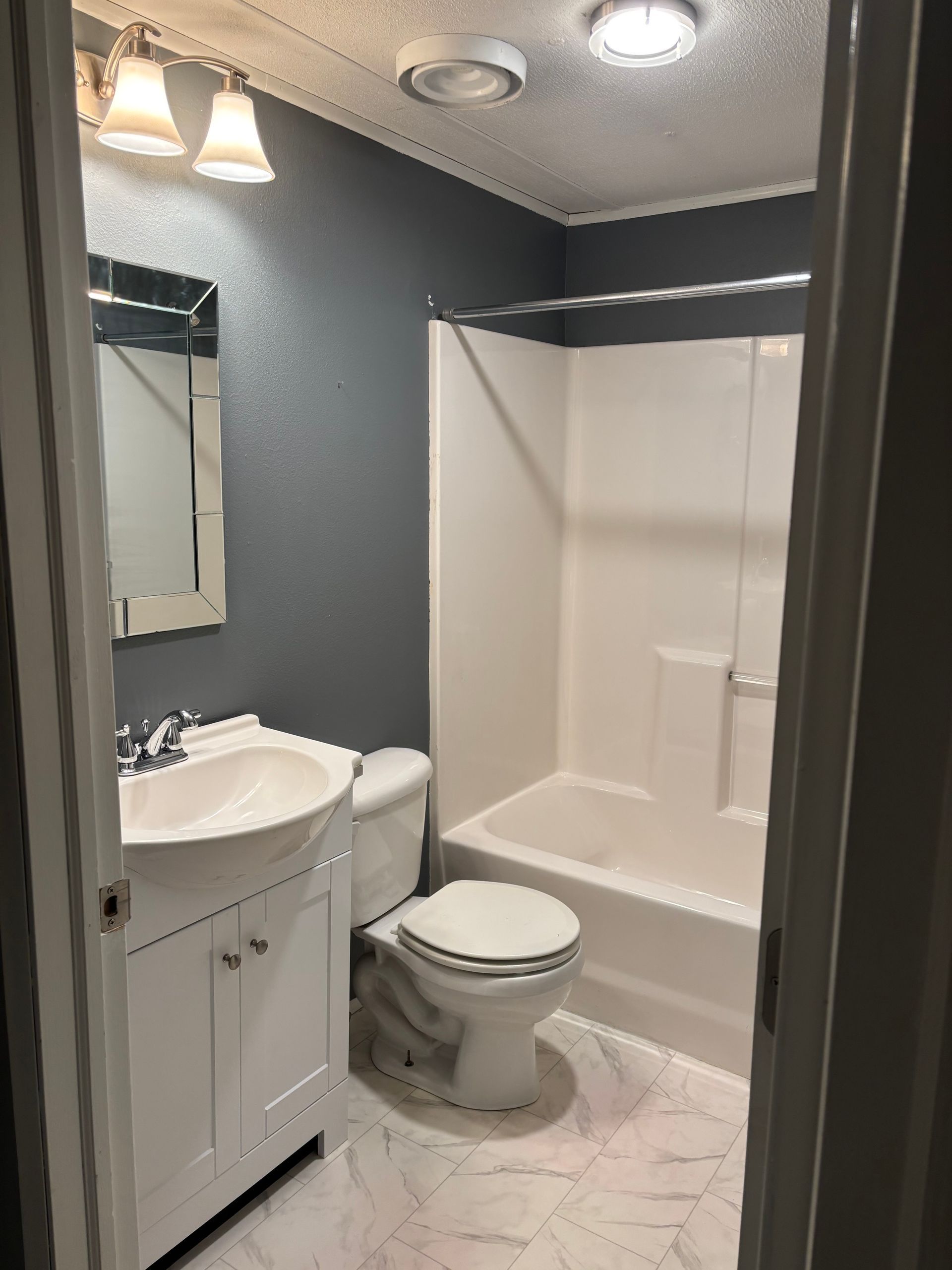 Bathroom with white fixtures, grey walls, and marbled flooring.