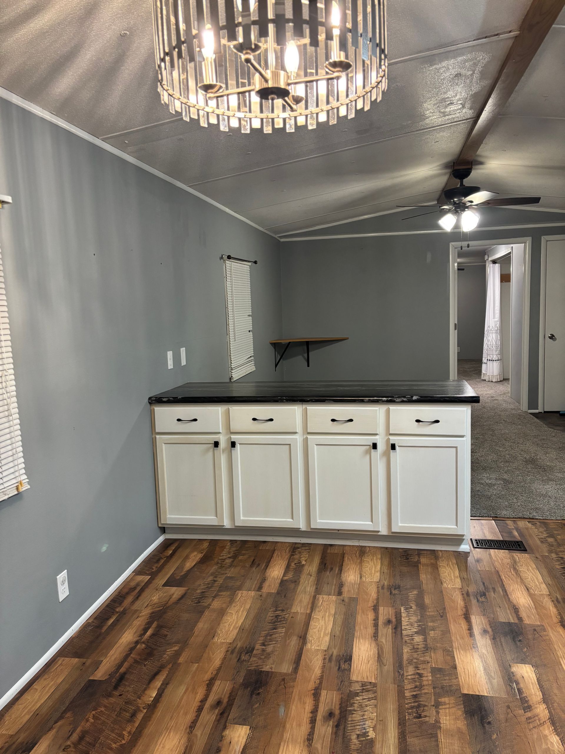 Interior of a home with wood-look flooring, white cabinets, grey walls, and a large chandelier.