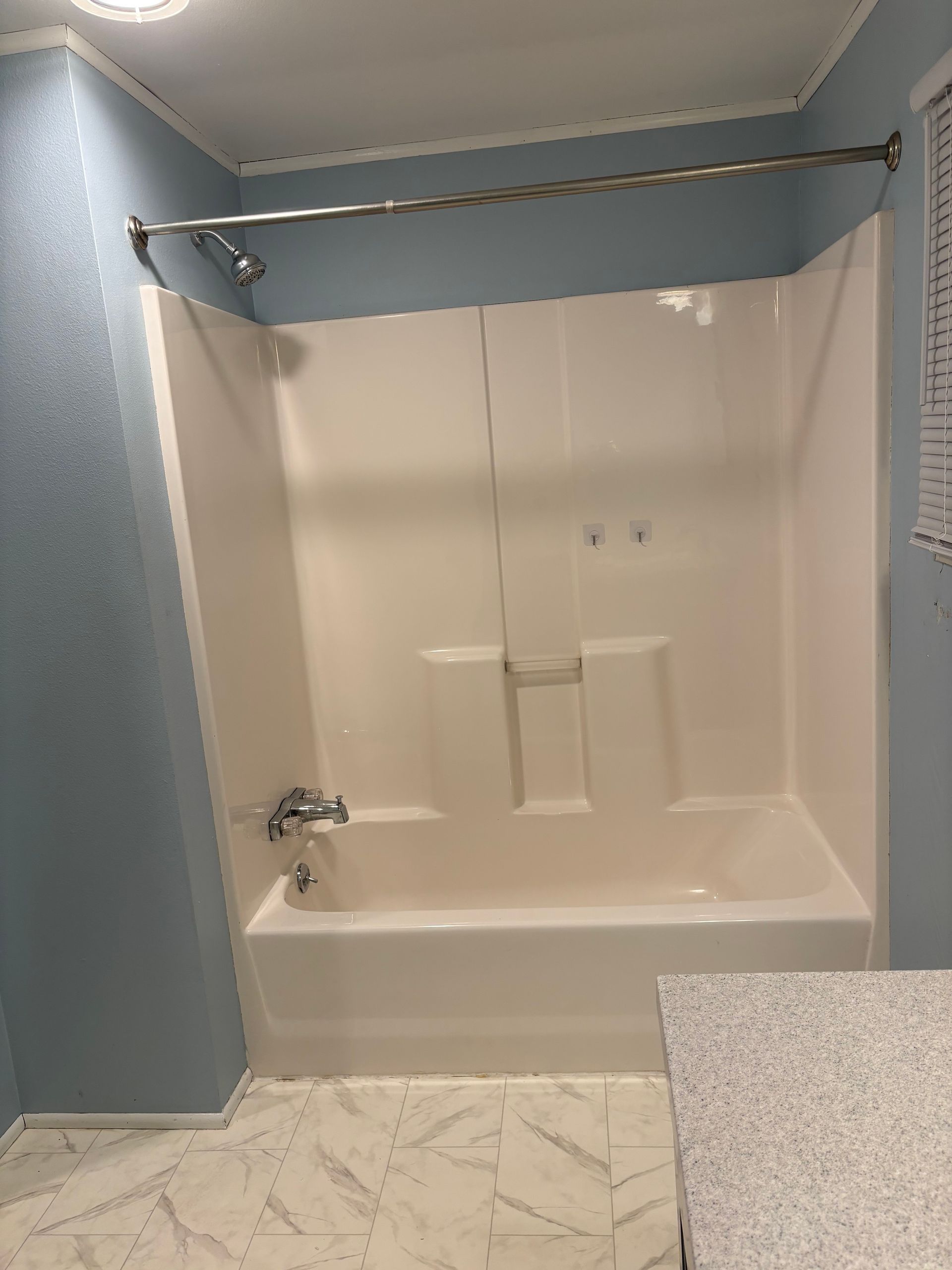 Bathroom with a white tub, shower walls, blue walls, and patterned floor.