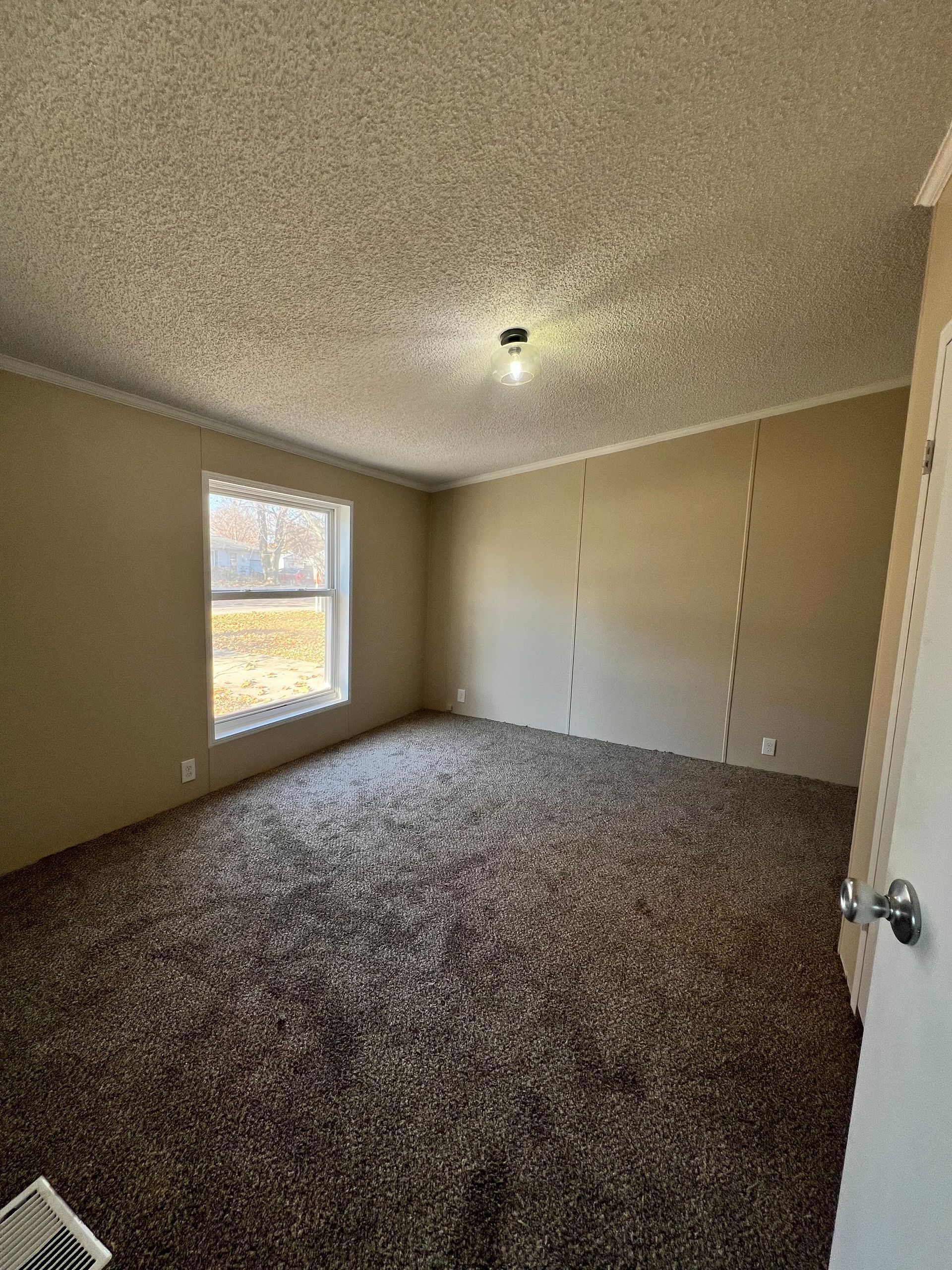 Empty room with brown carpet, tan walls, and a window.