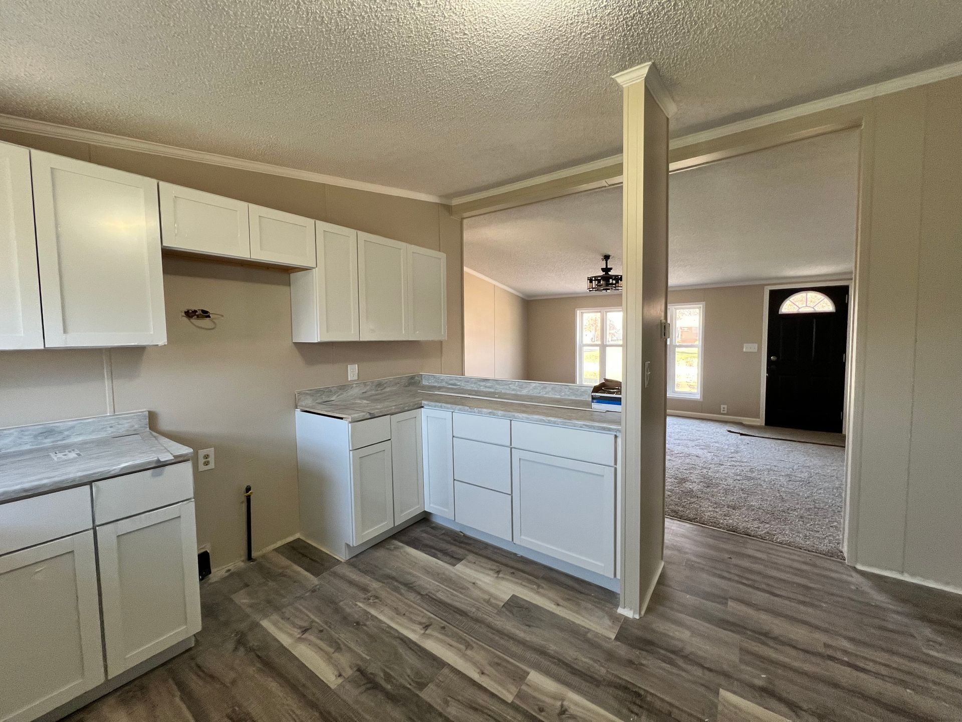 Kitchen with white cabinets, light countertops, and wood-look flooring. Entry to another room visible.