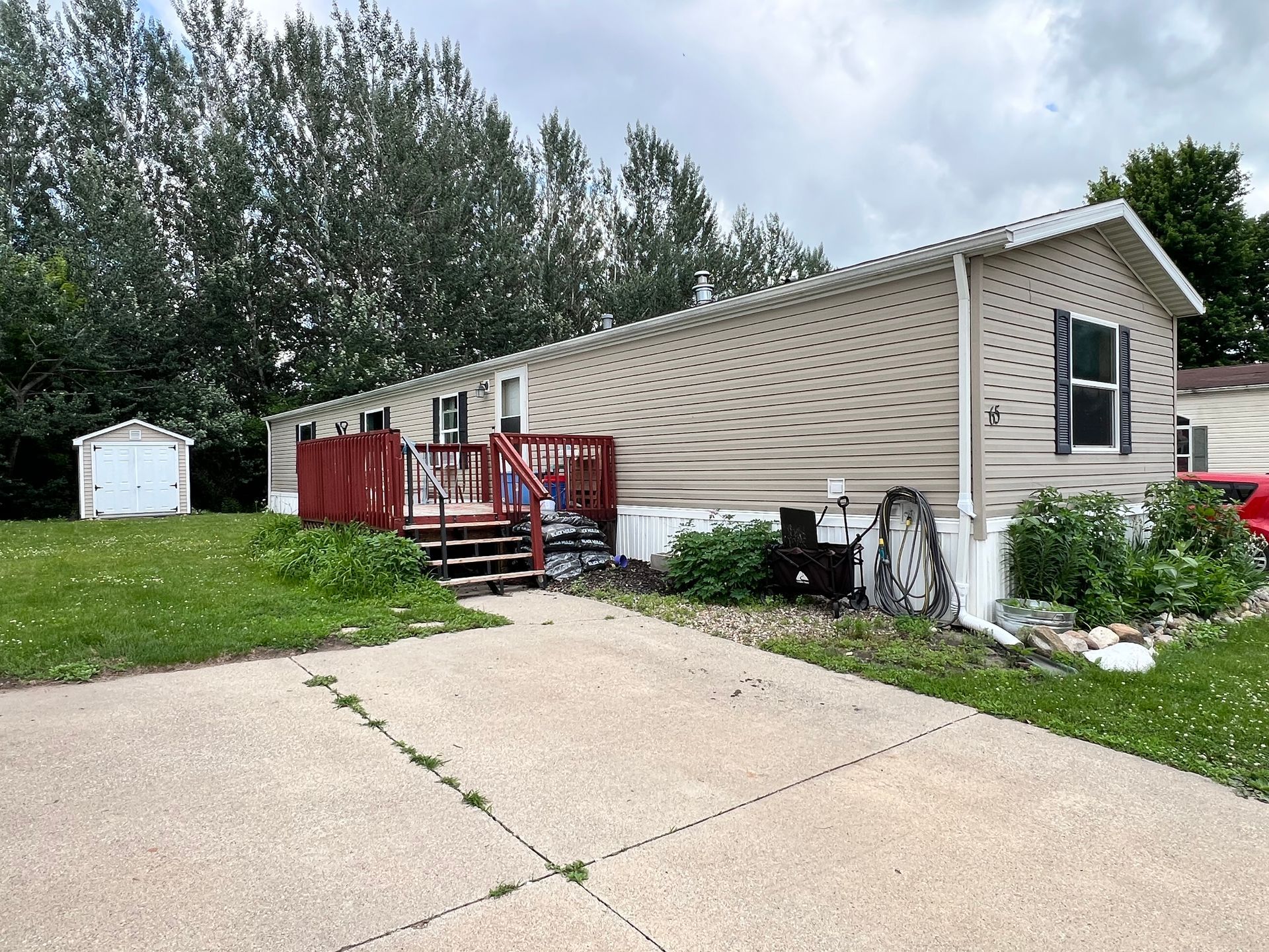Mobile home with white and gray siding, black deck and stairs, concrete driveway.