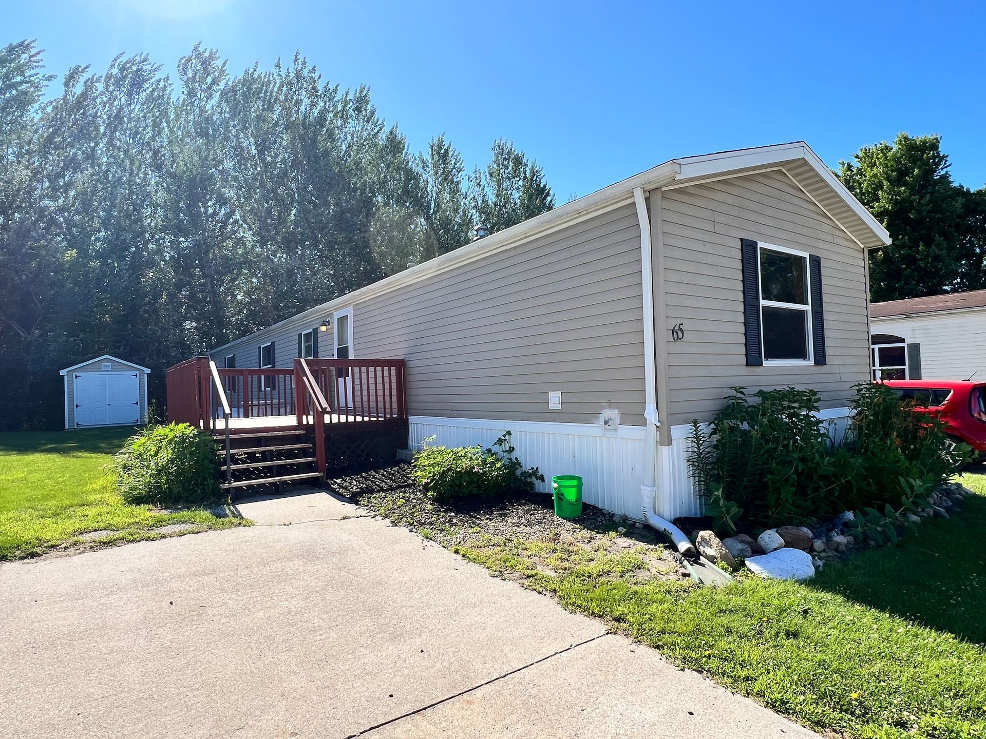 Mobile home with white and gray siding, black deck and stairs, concrete driveway.