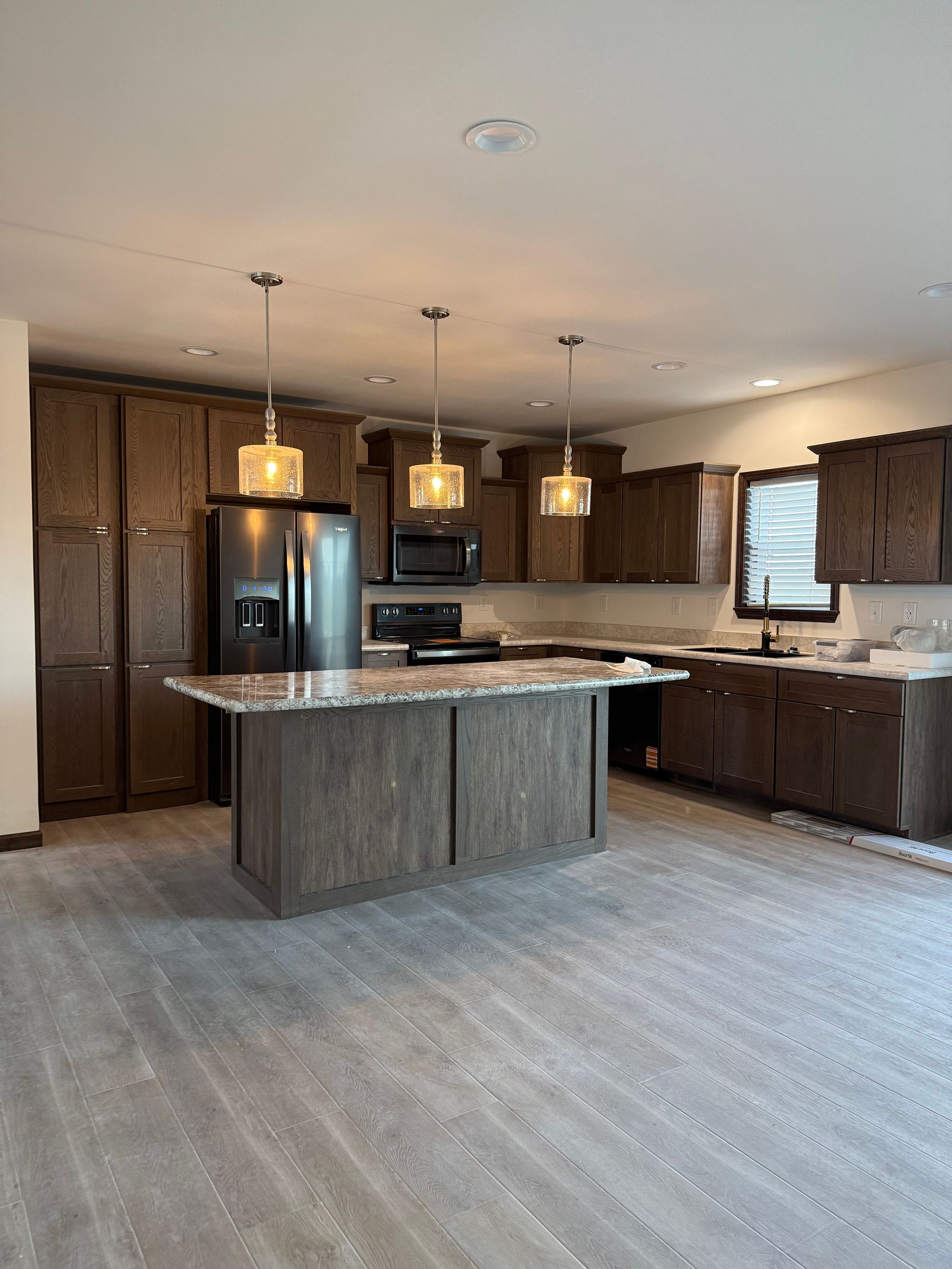 Brown-sided single-story house with white trim, door, and windows. Set on a foundation in a grassy field under a blue sky.
