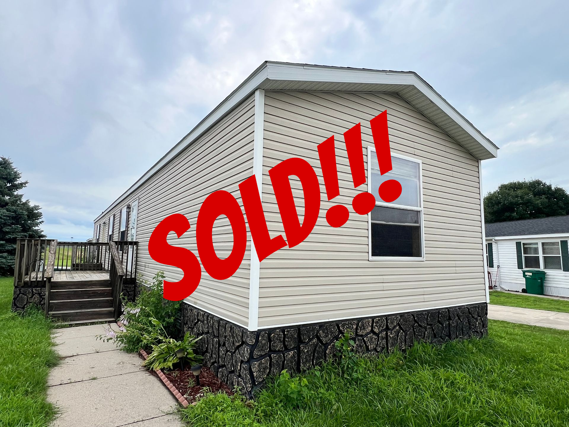 Tan mobile home with steps and a window, against a cloudy sky.