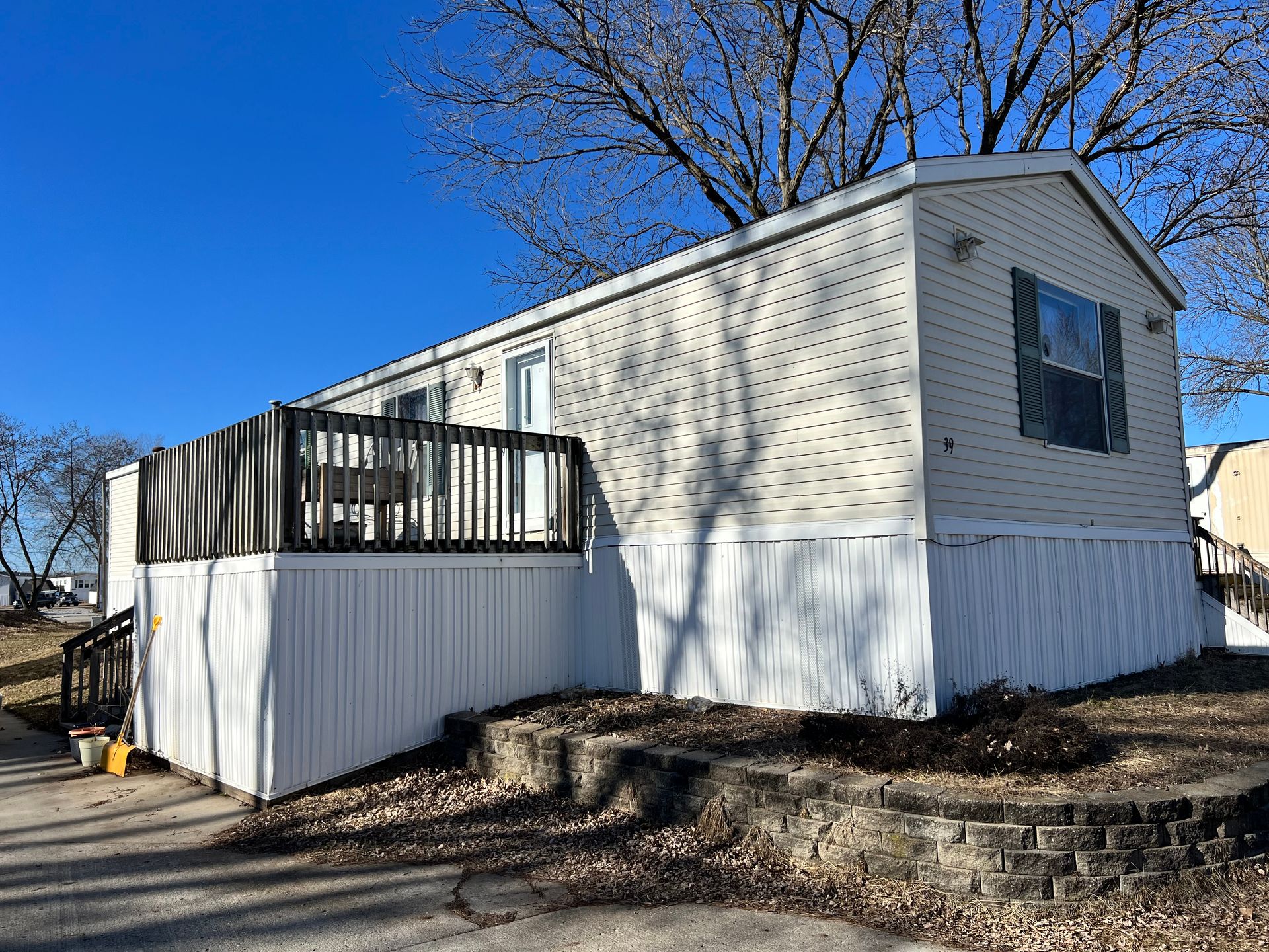 Mobile home with white and gray siding, black deck and stairs, concrete driveway.