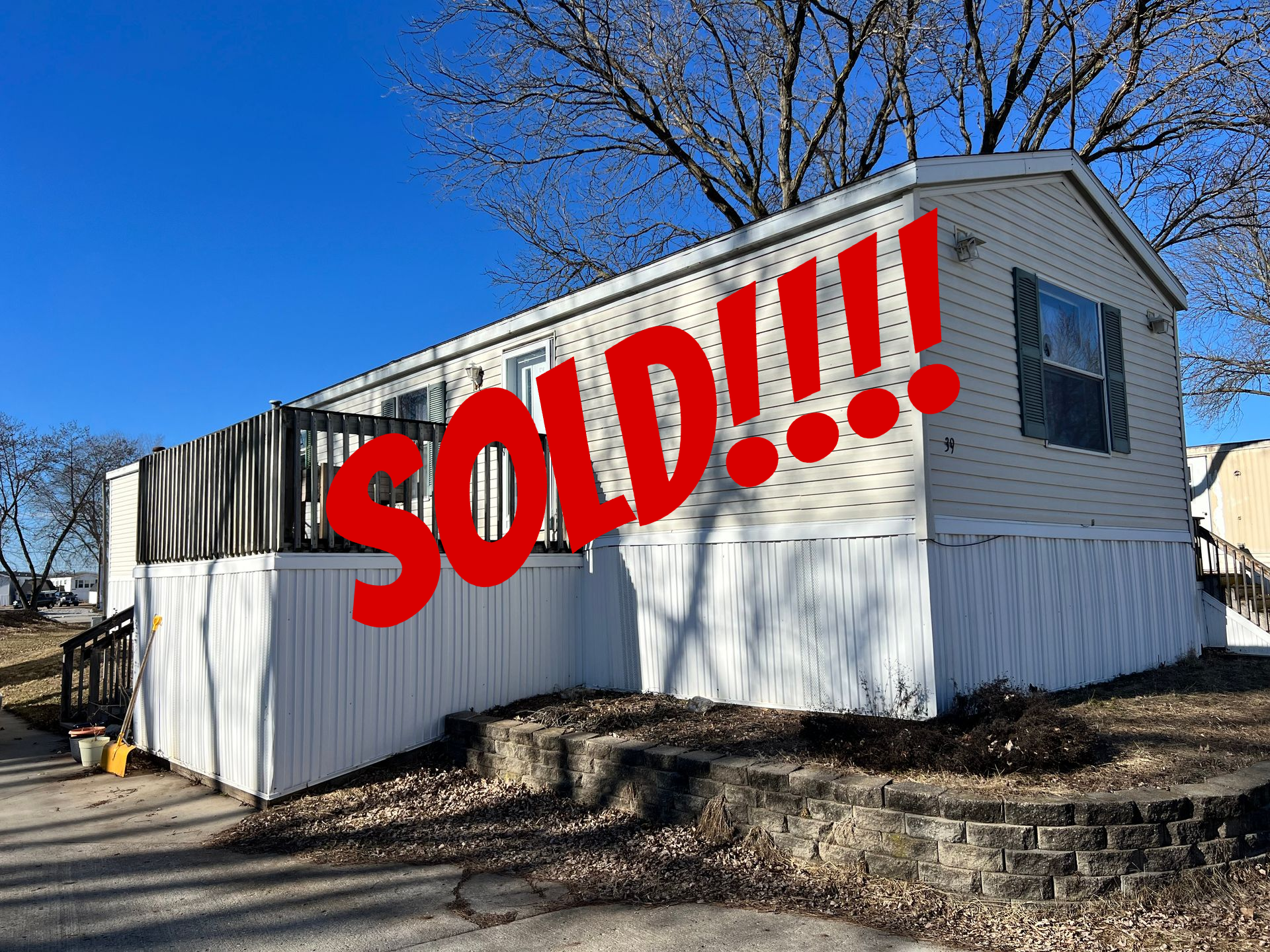 Mobile home with white and gray siding, black deck and stairs, concrete driveway.