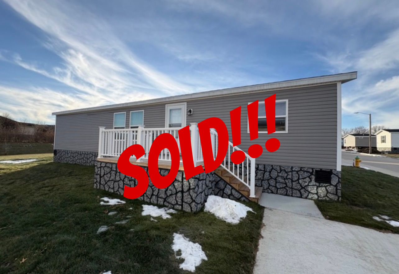Gray-sided, single-story house with white railing porch, stone-look base. Blue sky with clouds.