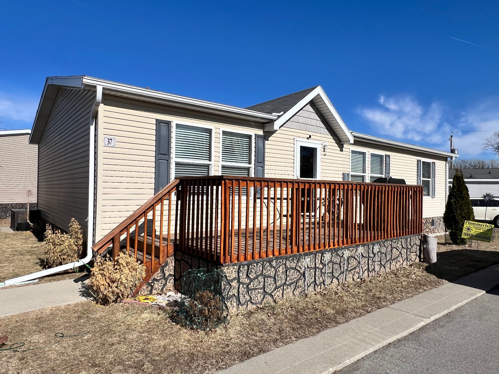 White mobile home with stone-patterned skirting and wooden steps leading to the front door.