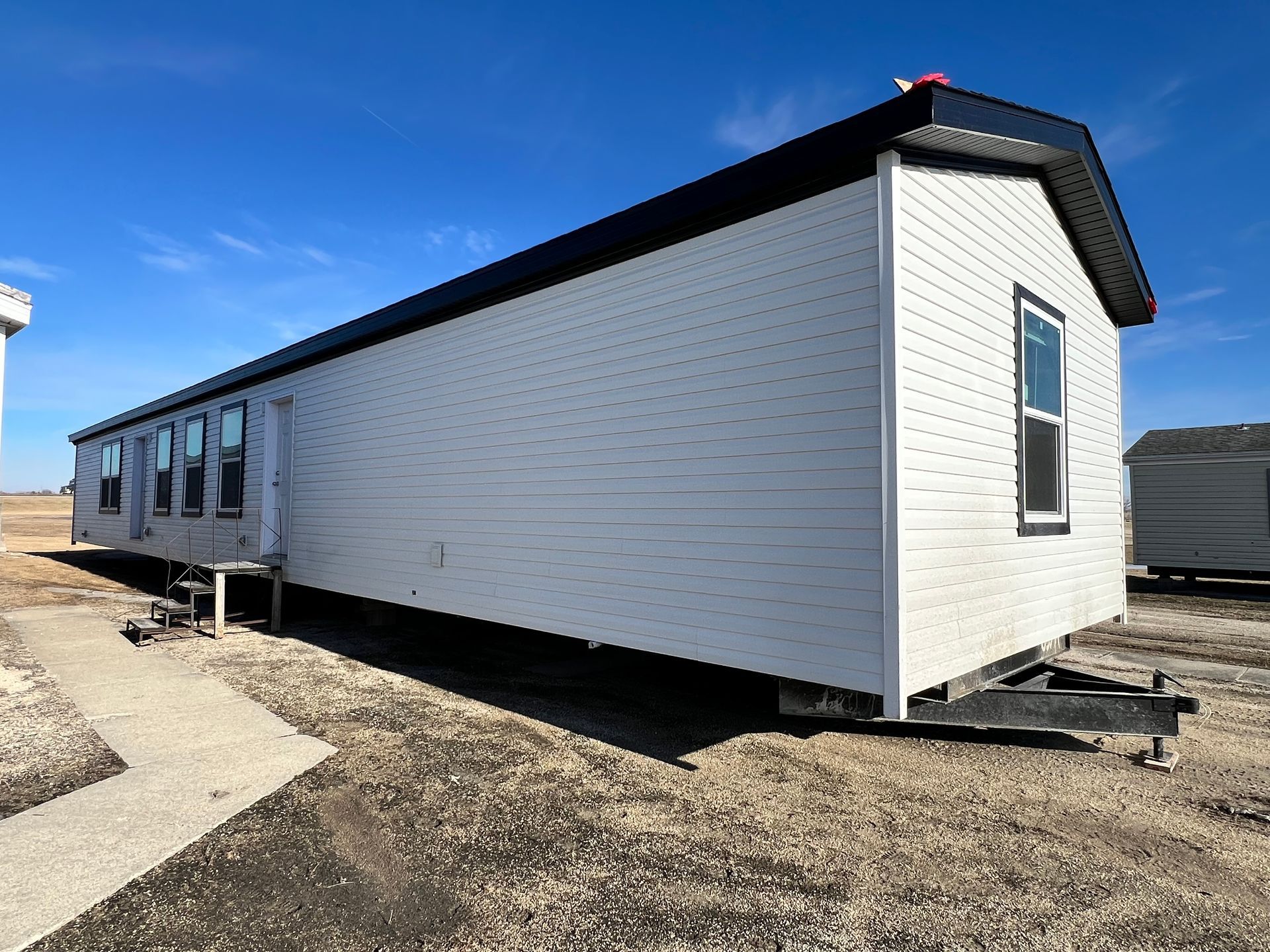 Tan mobile home with white trim on a snowy lot.