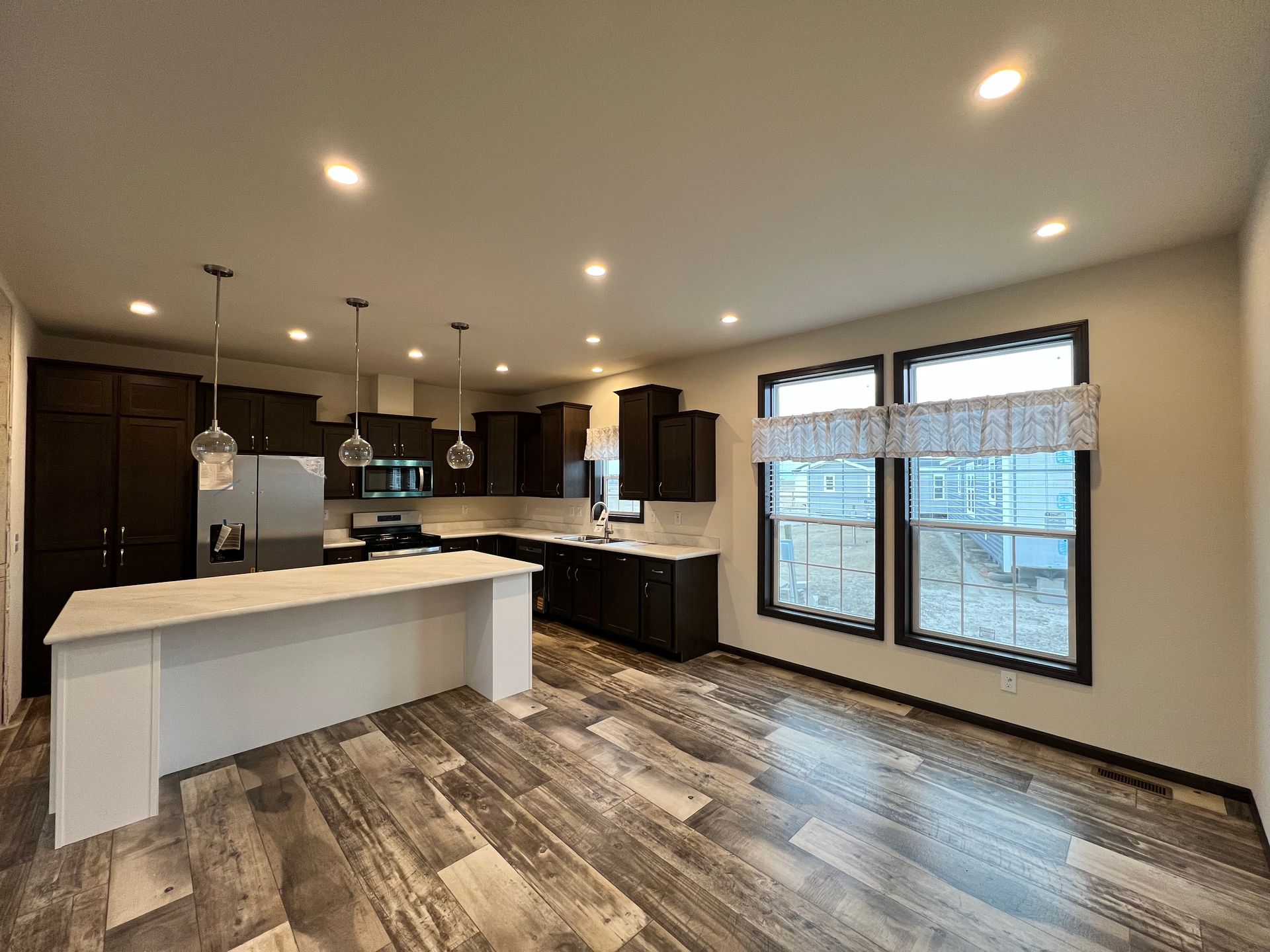 Brown-sided single-story house with white trim, door, and windows. Set on a foundation in a grassy field under a blue sky.