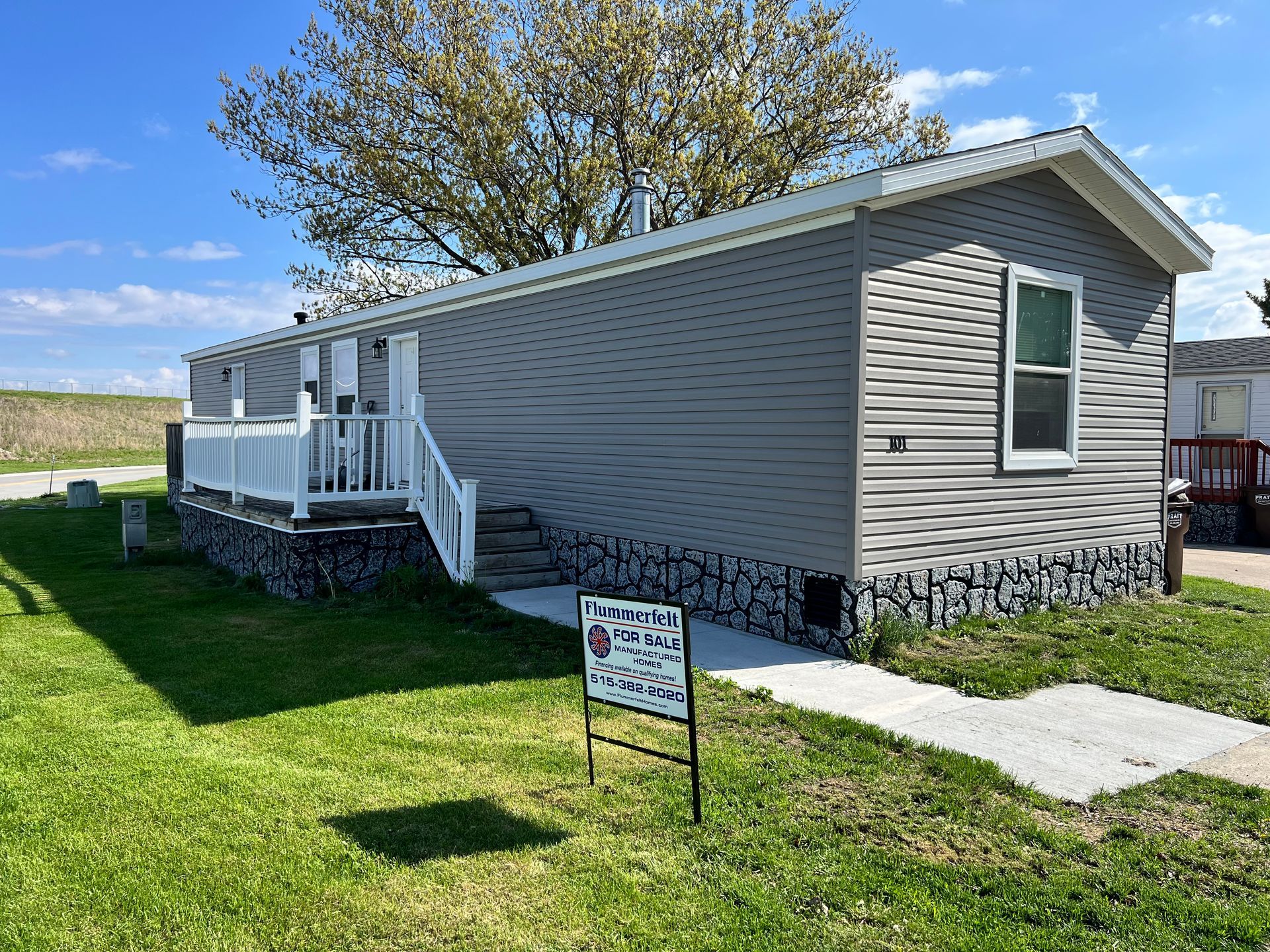 Tan mobile home with steps and a window, against a cloudy sky.