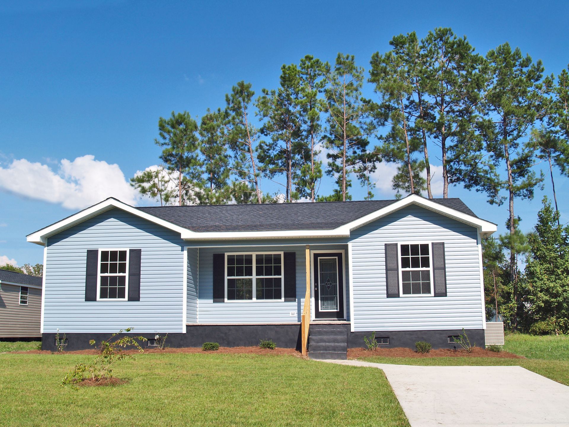 Light blue ranch home with black shutters, dark gray roof, and a concrete driveway.