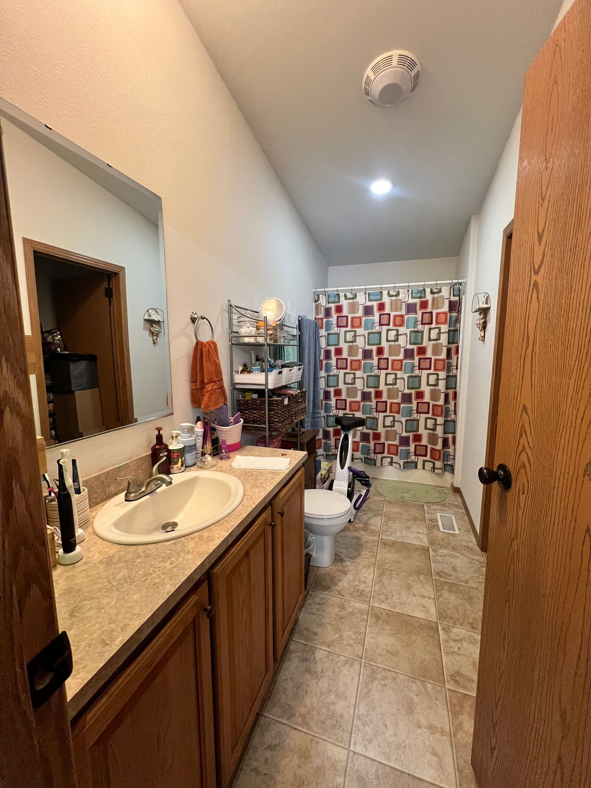 Bathroom with wood cabinets, tan countertop, and patterned shower curtain.