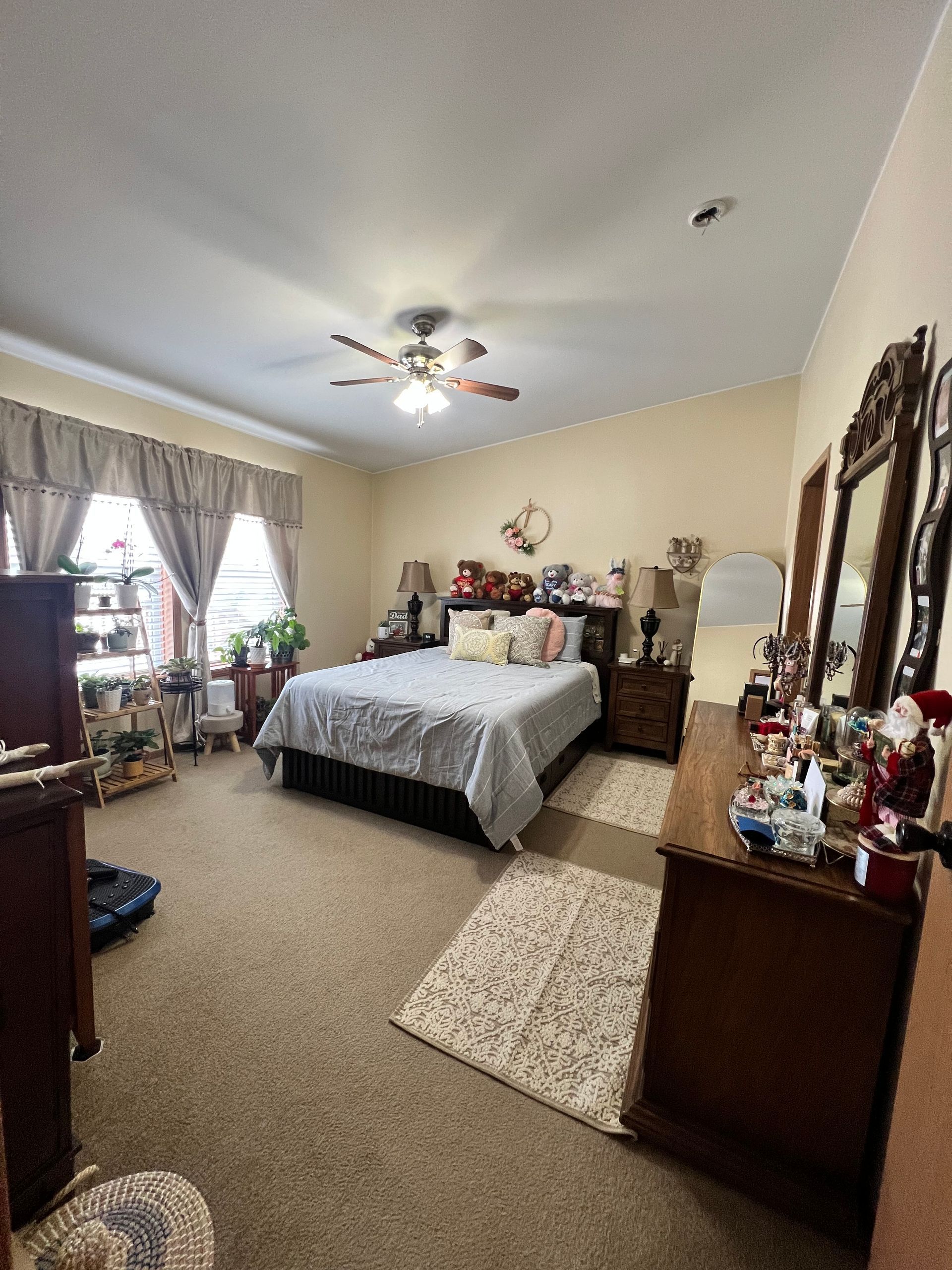 Bedroom with bed, dressers, mirrors, and window with curtains; brown carpet and neutral walls.