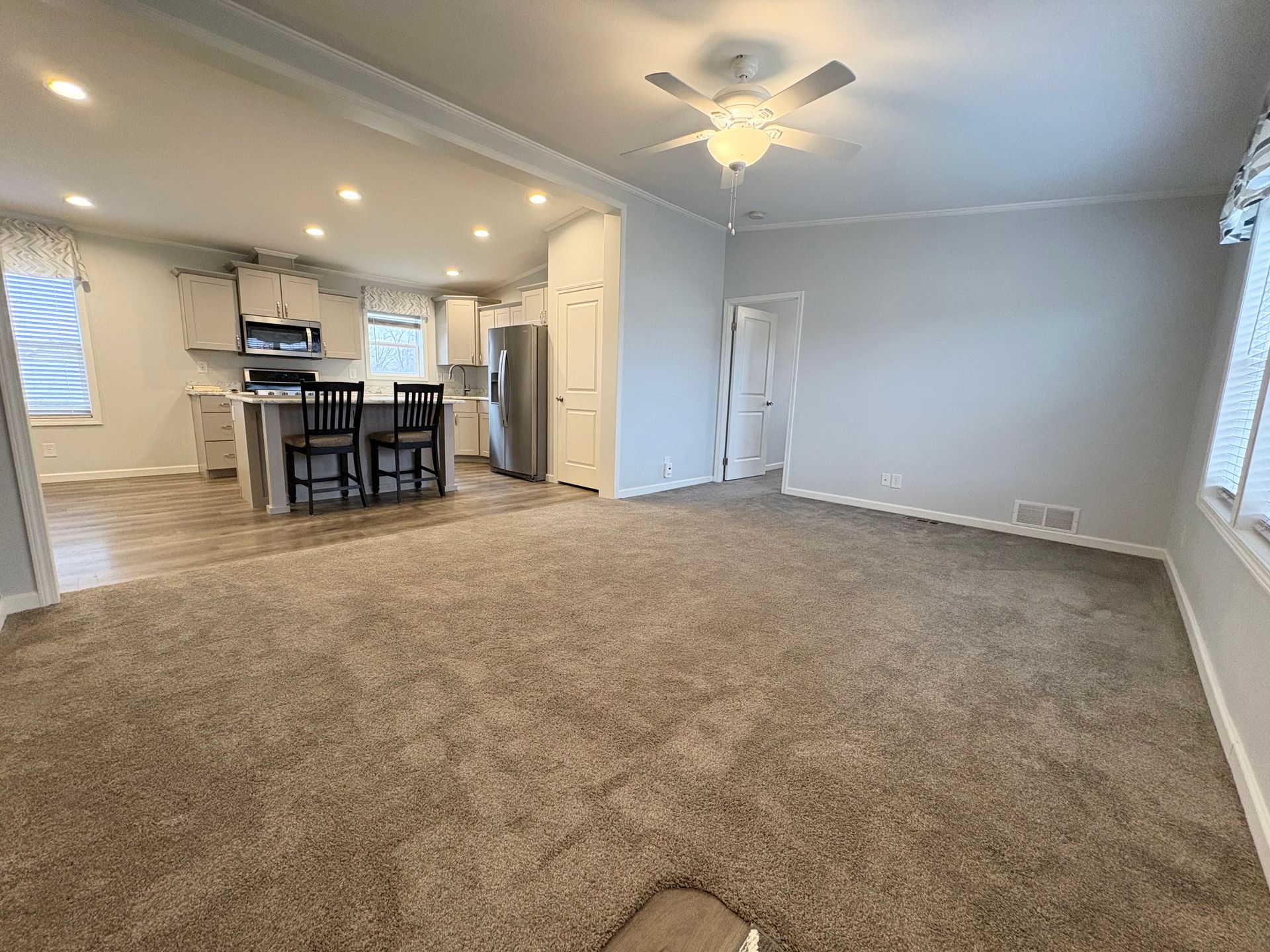 Open-concept living space with kitchen and living room; gray walls, beige carpet, and stainless steel appliances.